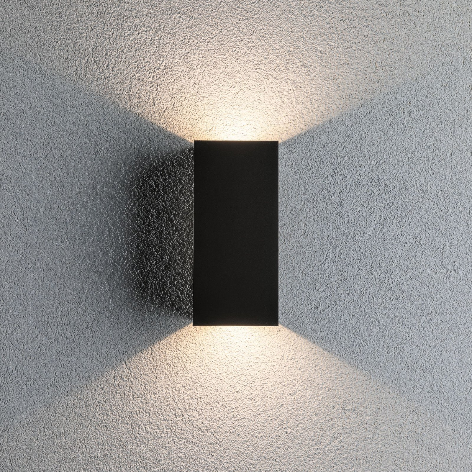 Czarna prostokątna lampa ścienna emitująca dwie wiązki światła na teksturowanej ścianie.