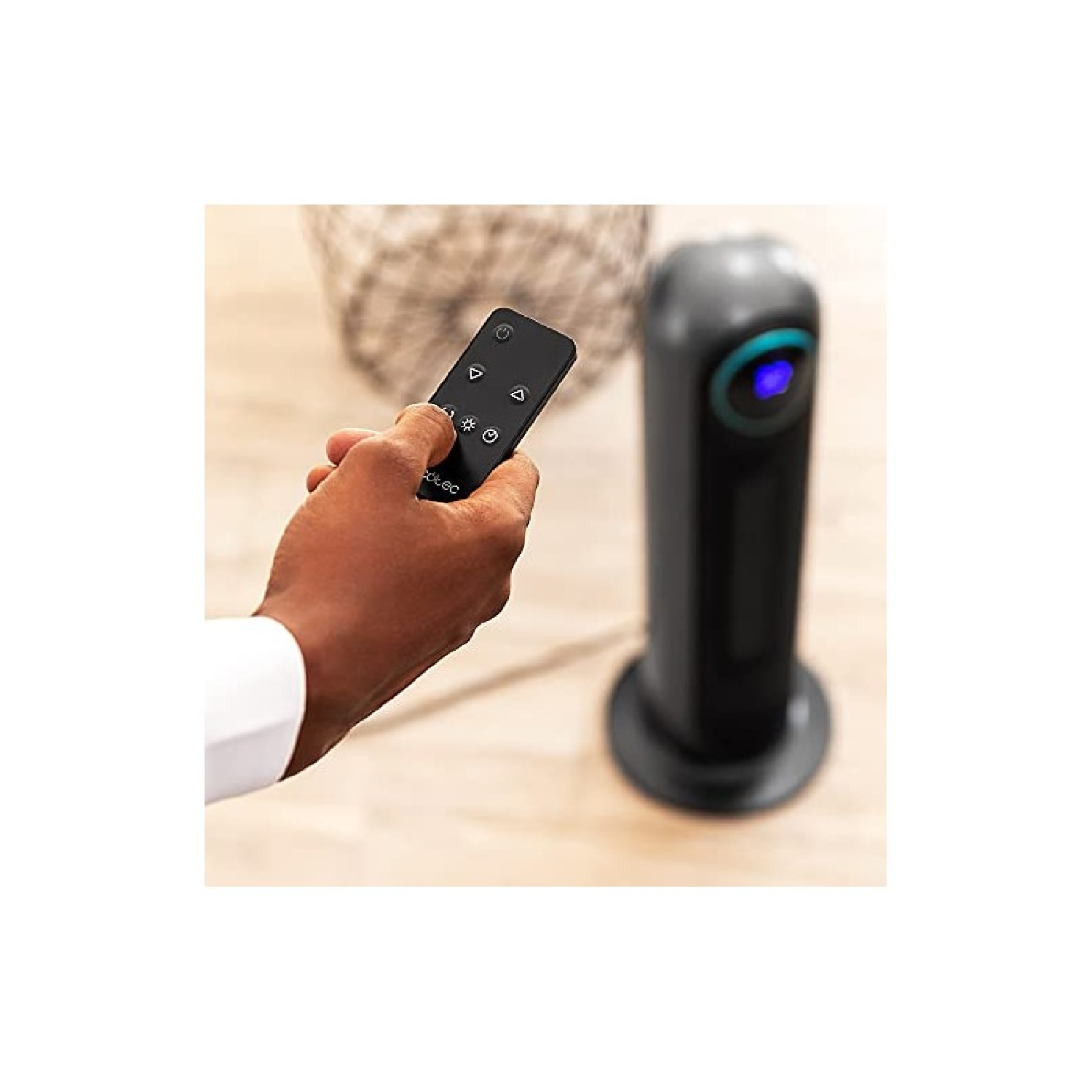 Dłoń trzyma pilota skierowanego na czarny, cylindryczny wentylator, na drewnianej powierzchni.