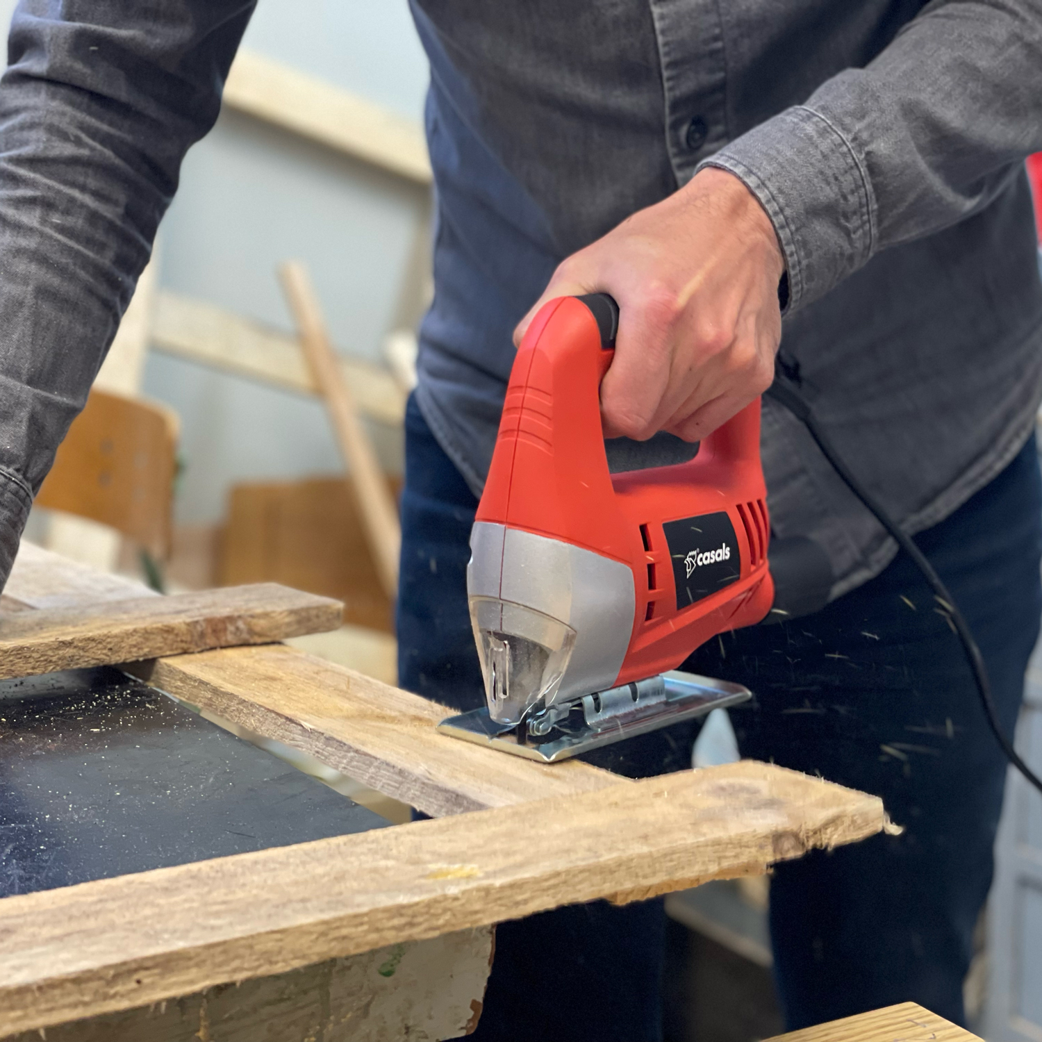 Una persona usando una sierra de calar roja para cortar madera, primer plano. La madera está en un banco de trabajo.