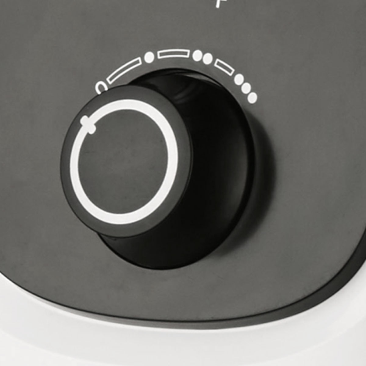 Zbliżenie czarnego pokrętła z białym oznaczeniem na szarej powierzchni, wskazujące ustawienia.