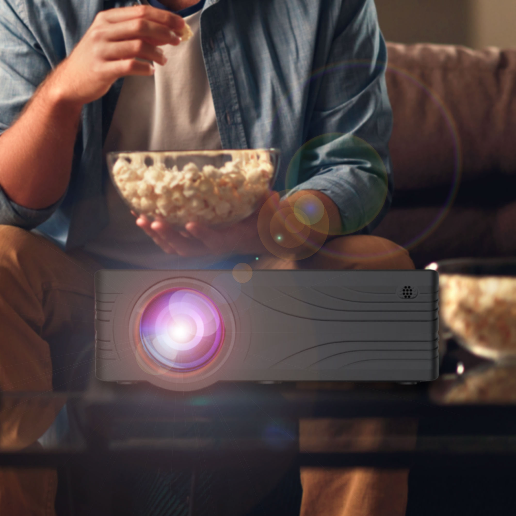 Ein Mann hält eine Schüssel Popcorn und schaut einen Film, der von einem Projektor auf einem Tisch gezeigt wird.