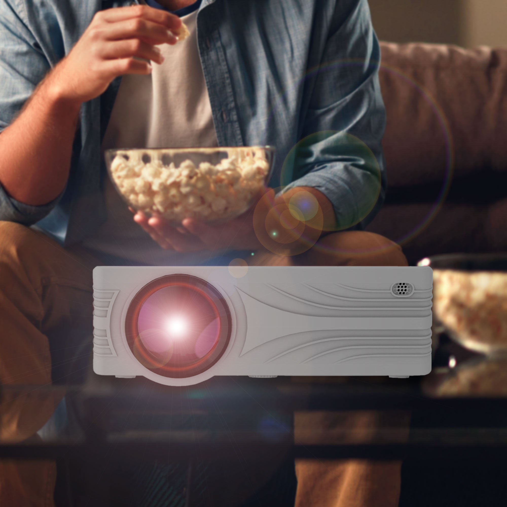 Ein Mann hält eine Schüssel Popcorn, mit einem Projektor im Vordergrund, der Licht projiziert.