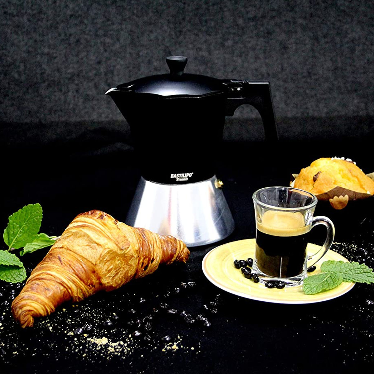 Kaffee mit Croissant und Muffin, mit Minze. Schwarzer Hintergrund, mit Kaffeemaschine.