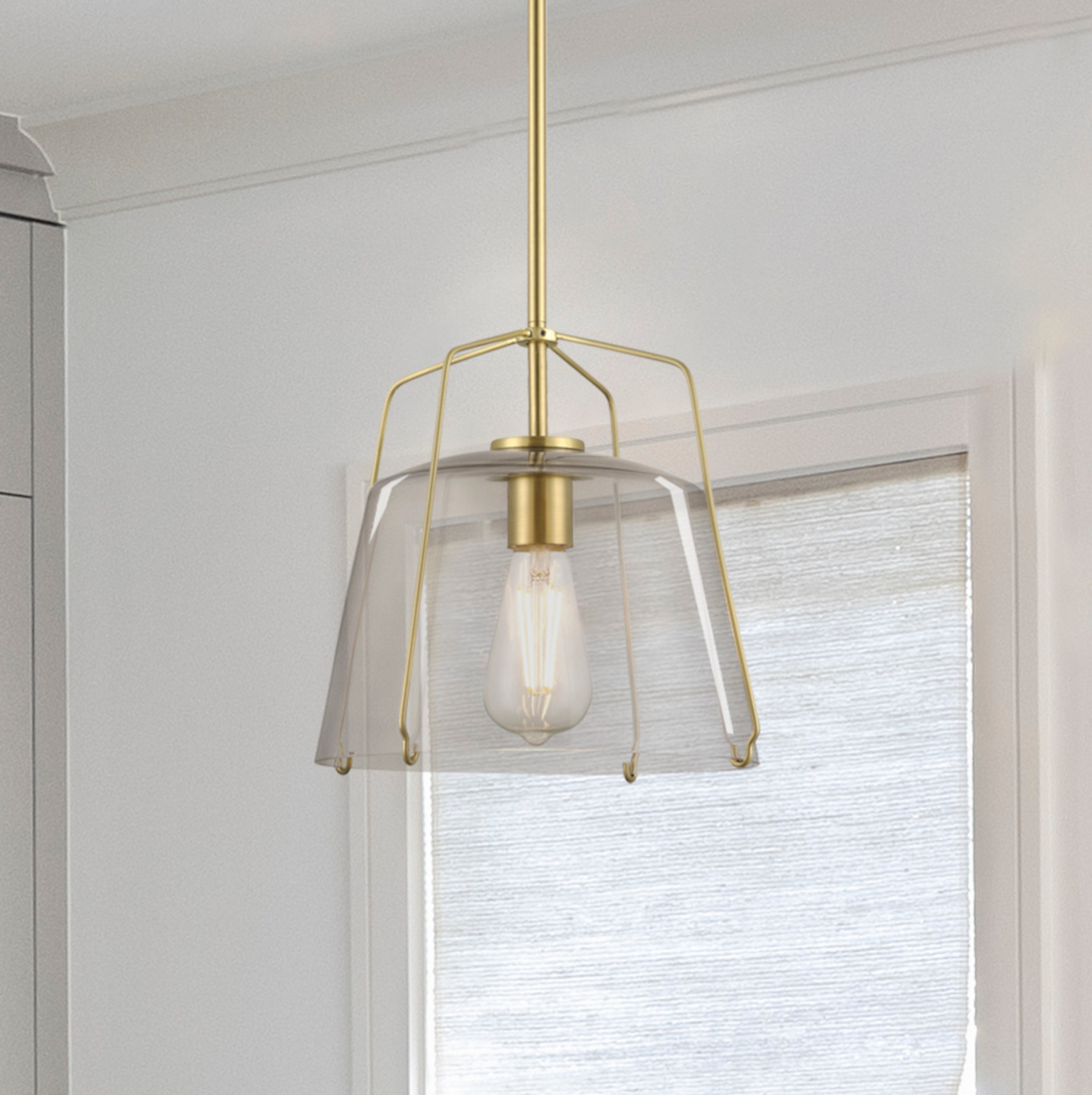 Eine goldene Pendelleuchte mit einem klaren Glasschirm und einer sichtbaren Glühbirne. Es ist in einer Küche.