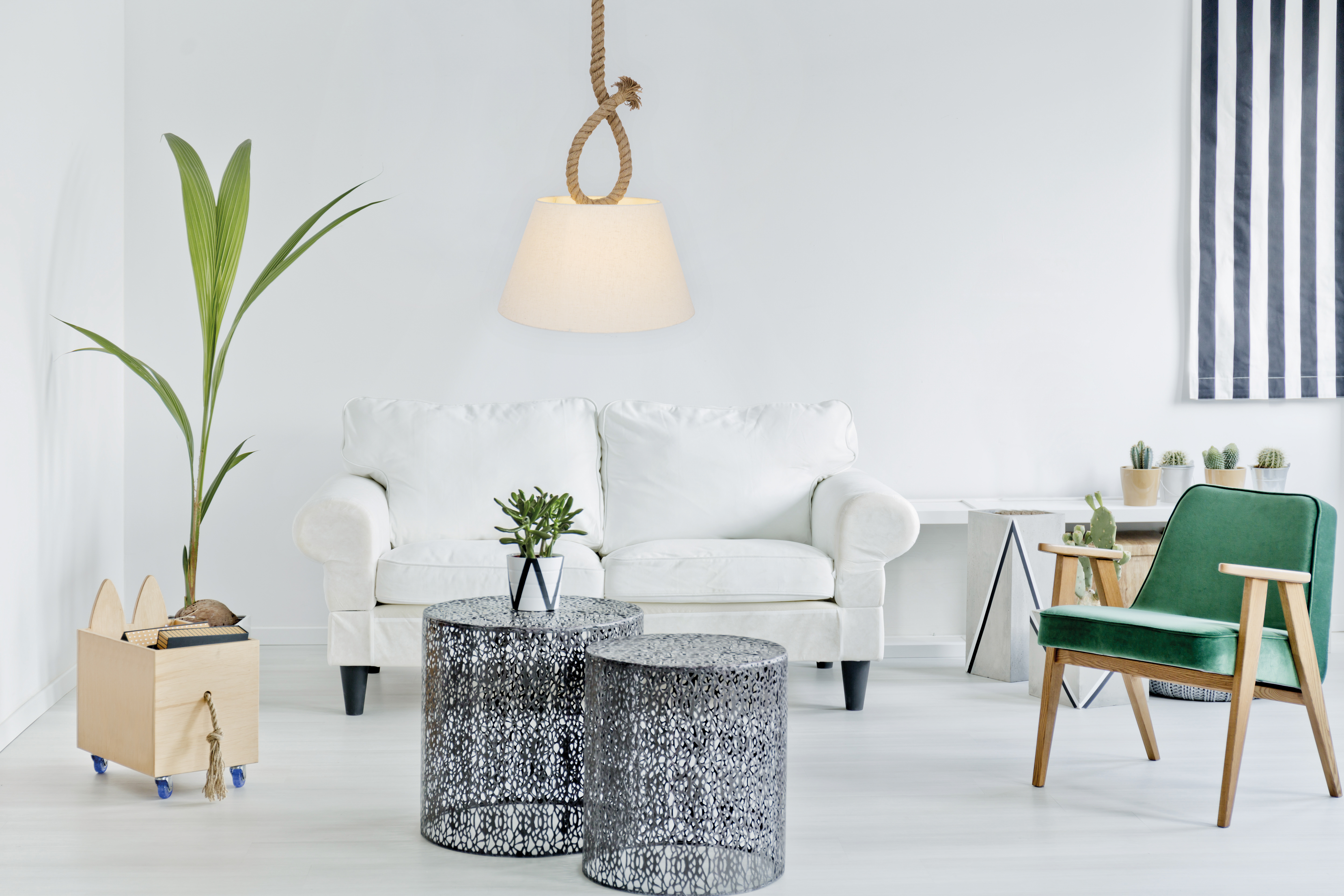 Ein modernes Wohnzimmer mit weißem Sofa, zwei Tischen, einem grünen Stuhl und einer Pflanze.