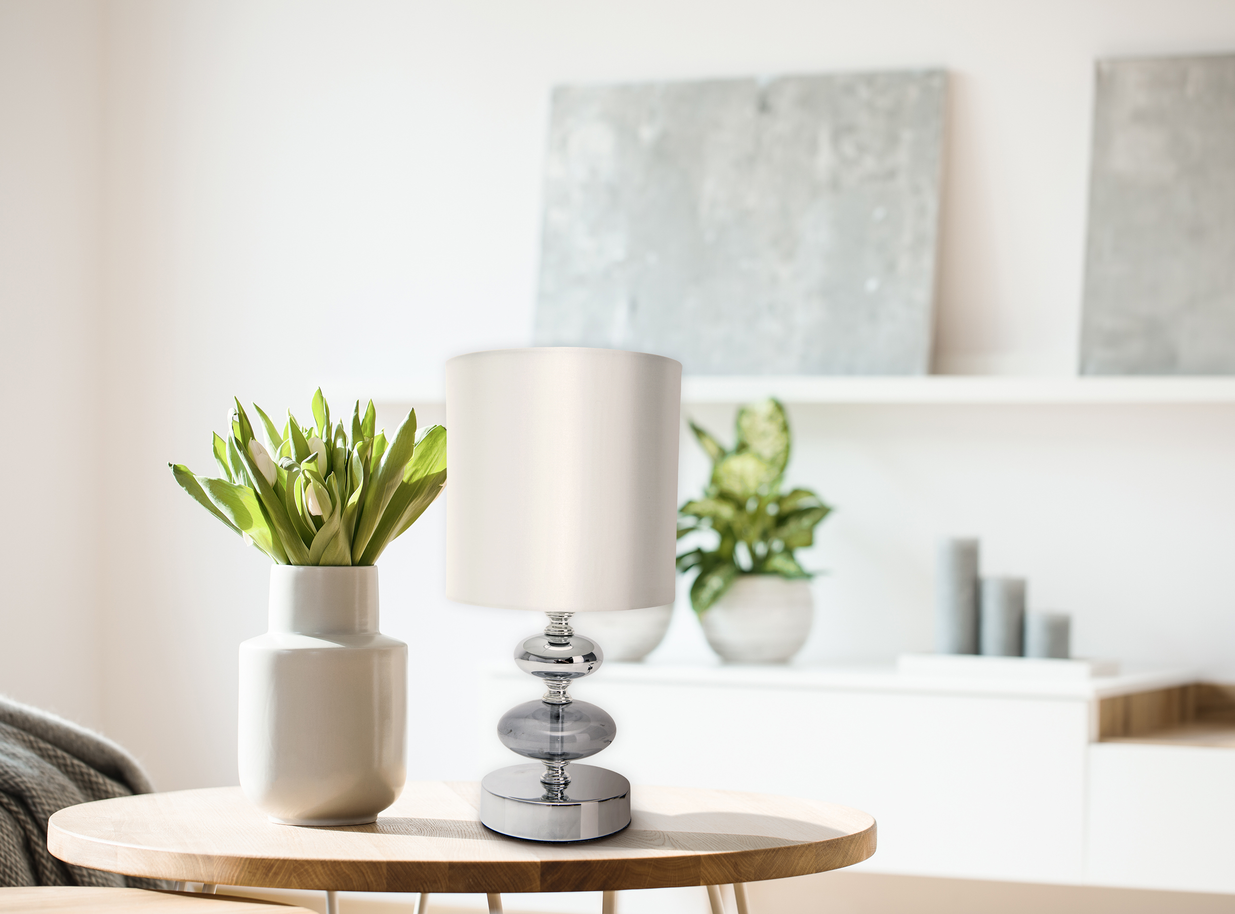 Eine Lampe auf einem Tisch neben einer Blumenvase und einem Fenster.