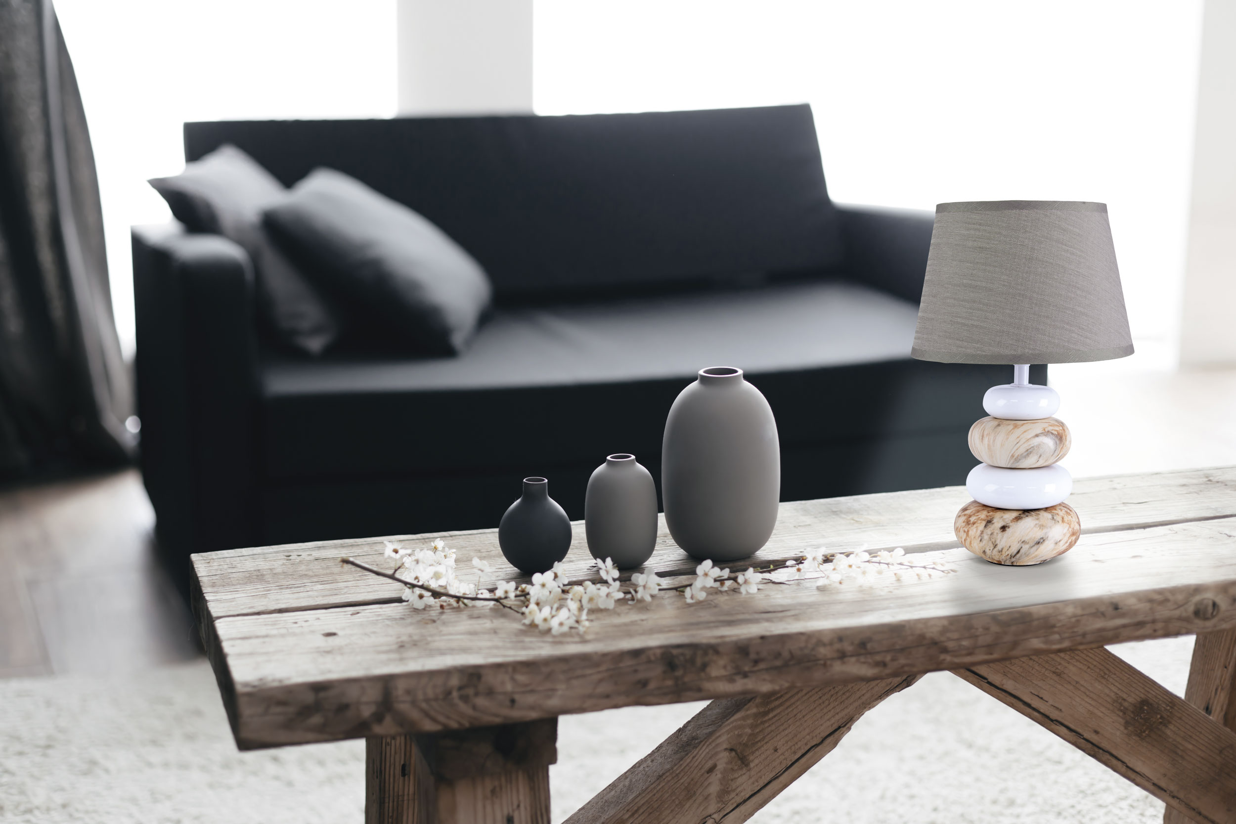 Innenaufnahme: Couchtisch mit Vasen, Blumen und einer Lampe in der Nähe eines Sofas.