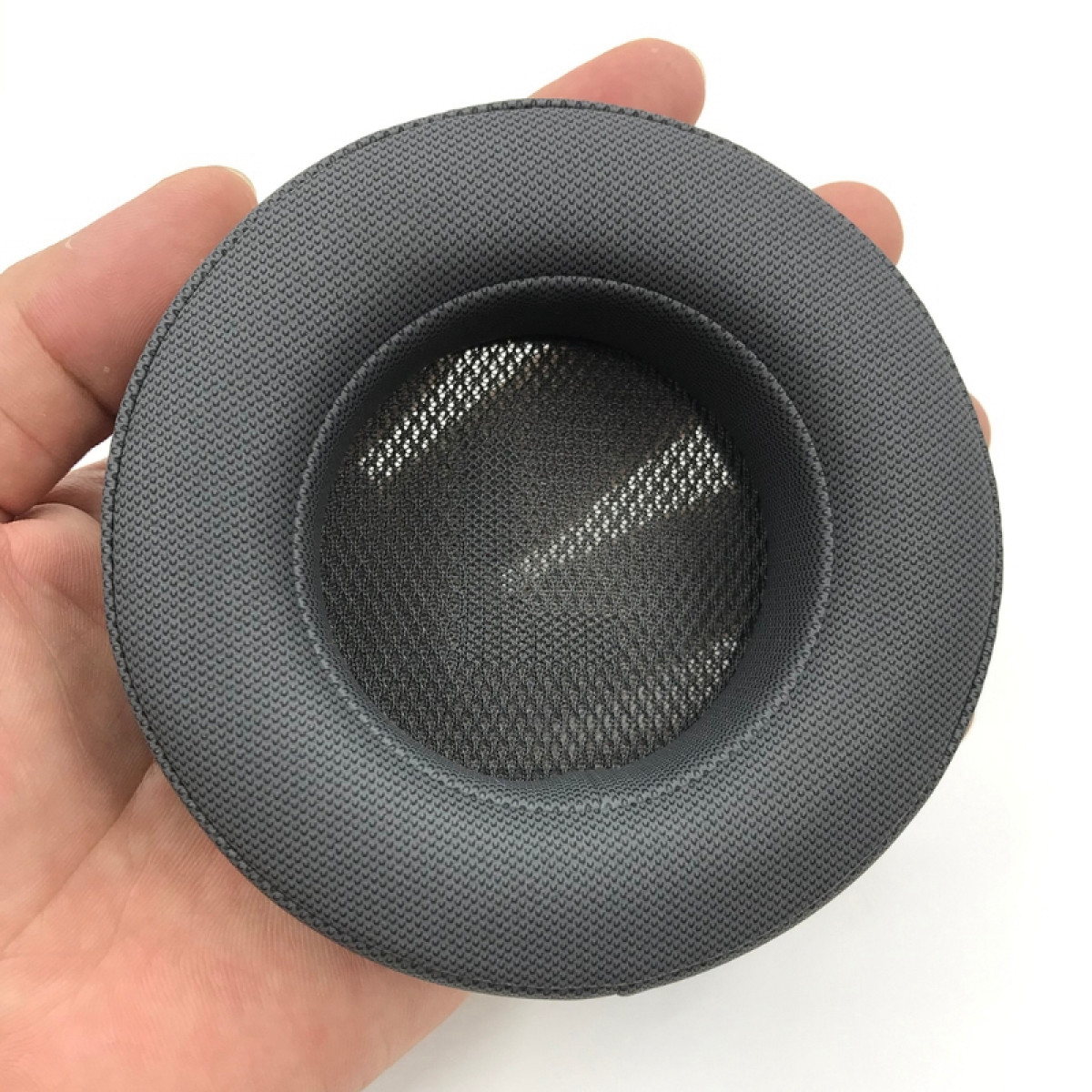 Almohadilla gris de auriculares sostenida por una mano, primer plano sobre fondo blanco.