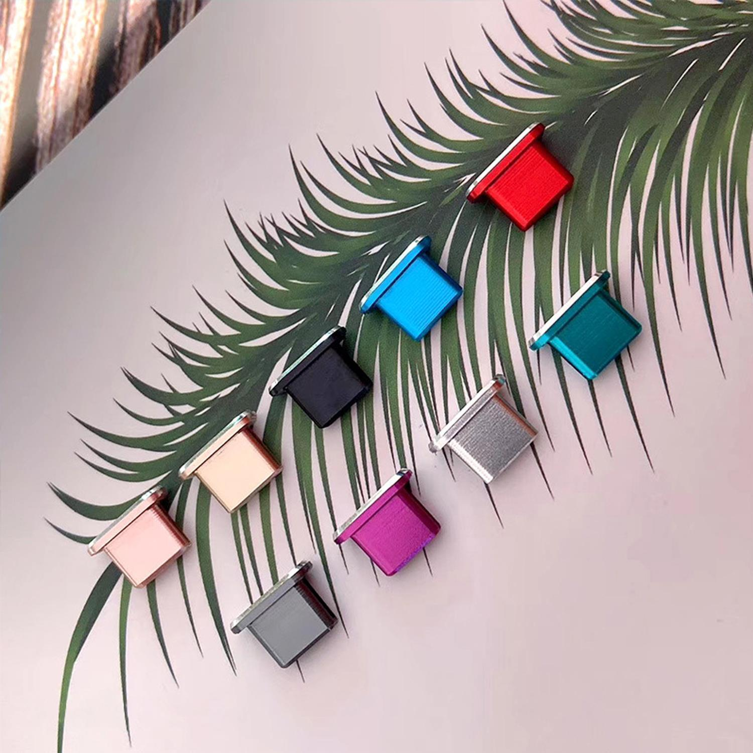 Una collezione di tappi antipolvere colorati per porte del telefono, disposti su una superficie coperta di foglie.