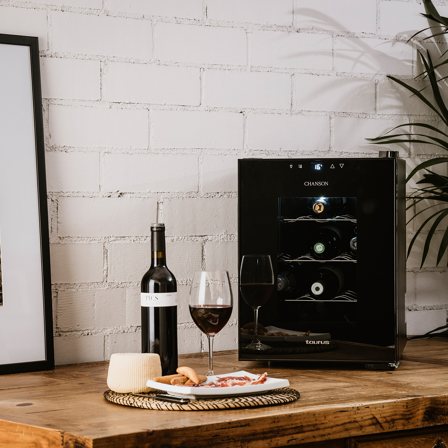 Una vinoteca con una botella de vino tinto, dos copas y aperitivos sobre una mesa de madera.