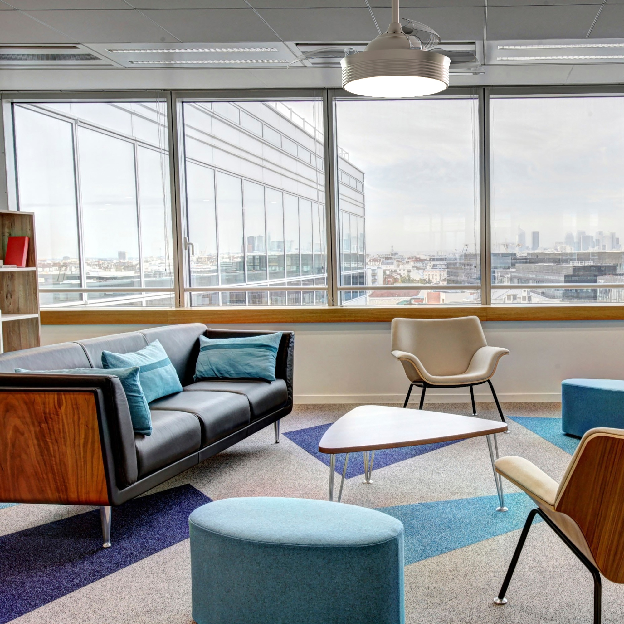 Interior de oficina moderno con sofá negro, cojines azules y sillones neutros junto a una gran ventana.