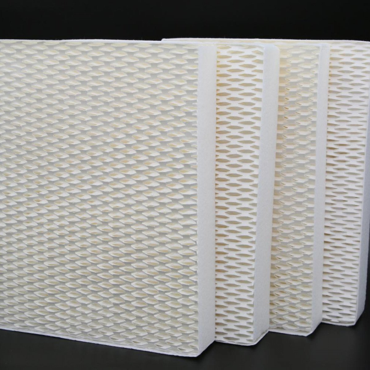 Cztery ułożone w stos białe filtry nawilżacza z wzorem plastra miodu i czarnym tłem.