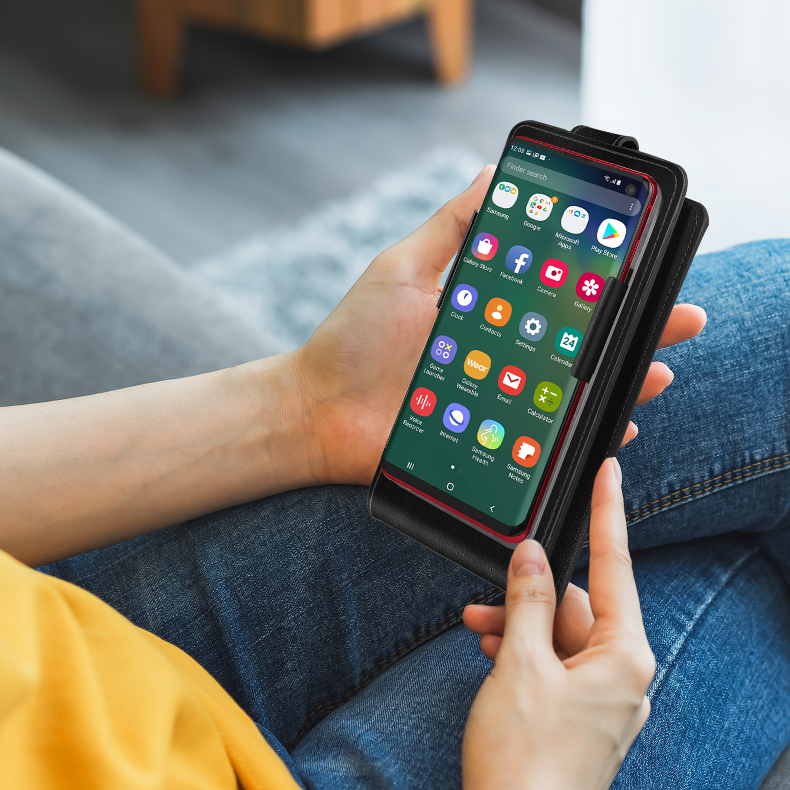 Una persona tiene in mano un telefono con una custodia che mostra una schermata dell'app. Lo sfondo è un divano.