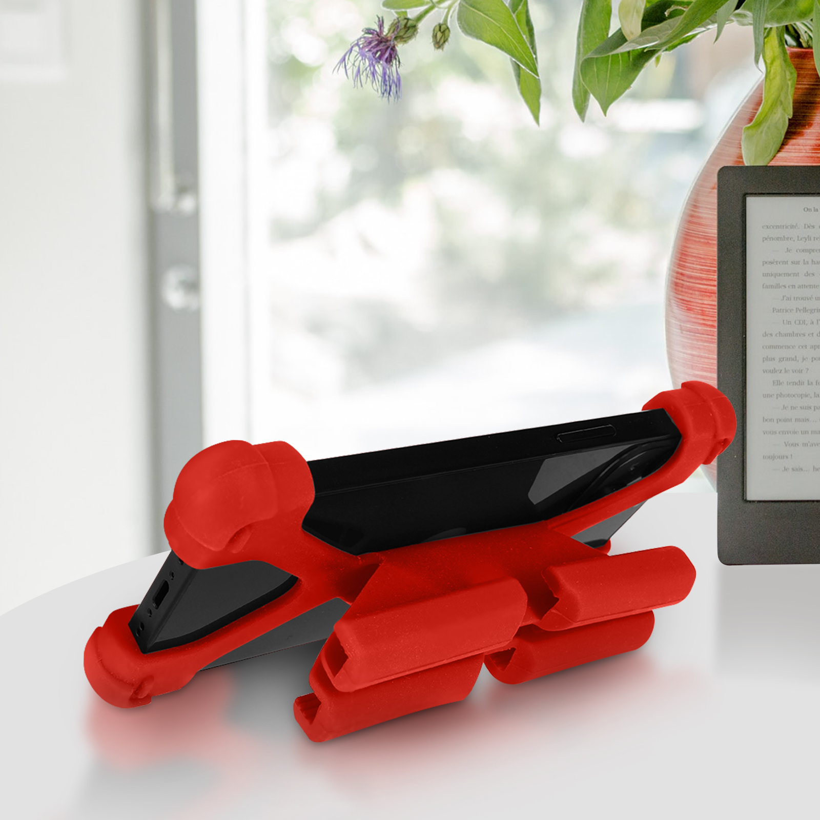 Roter Telefonhalter mit Telefon, vor einer Vase mit Blumen und einem Buch.
