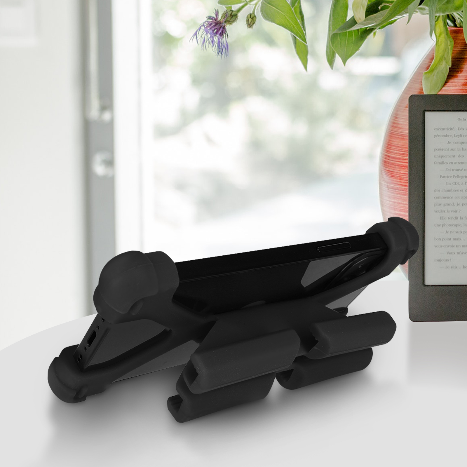 Schwarze Handyhülle mit Ständer auf weißem Tisch. Ein Fenster und eine Vase sind im unscharfen Hintergrund.
