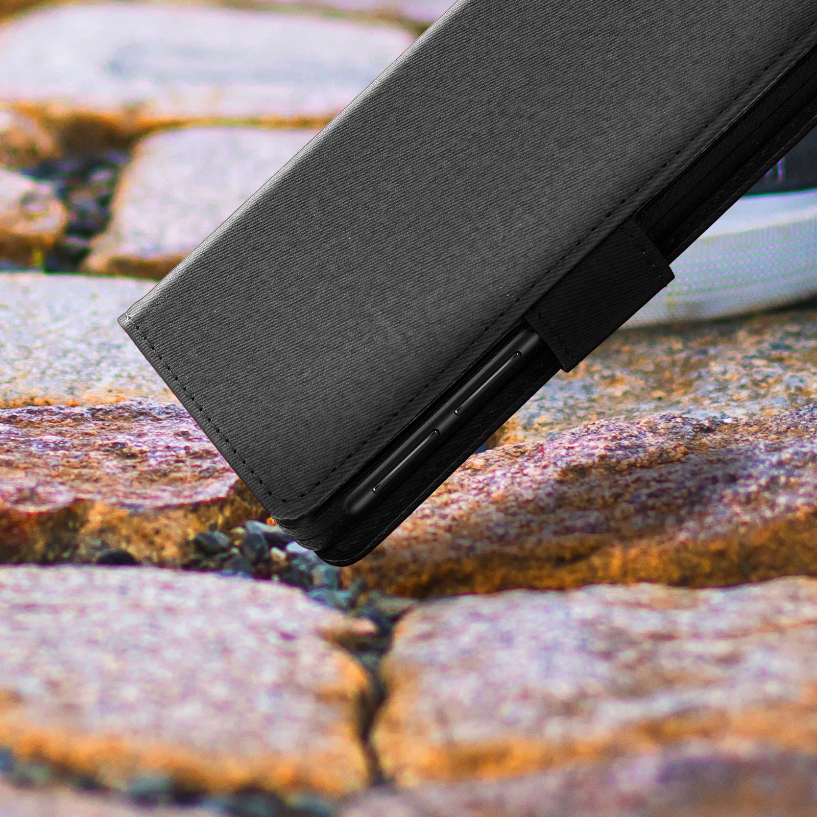 Eine schwarze, strukturierte Handyhülle mit einem Stift, der auf einer rauen Steinoberfläche liegt.
