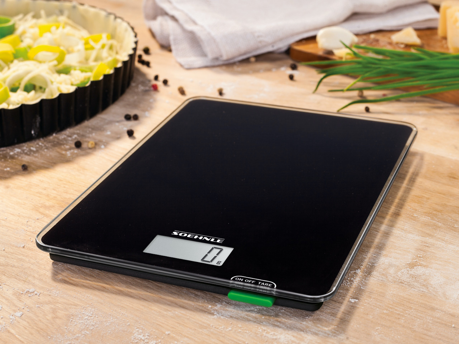 Czarna cyfrowa waga kuchenna z czarną powierzchnią, widoczny proces przygotowywania jedzenia.