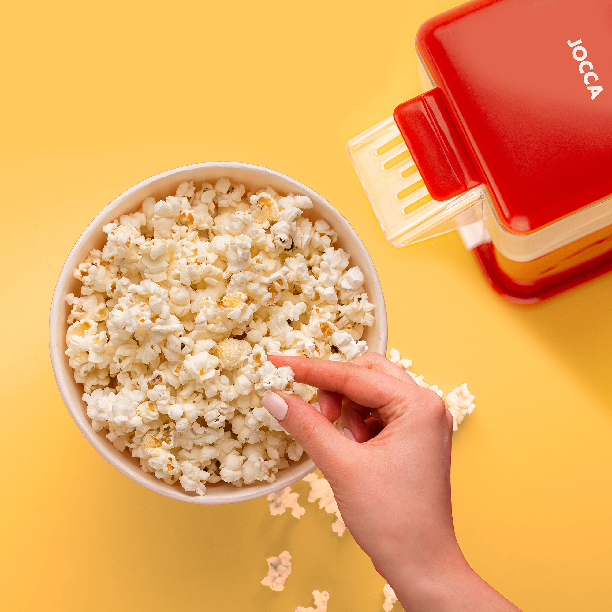 Donna che prende popcorn da una ciotola. Macchina per popcorn sullo sfondo. Sfondo giallo.