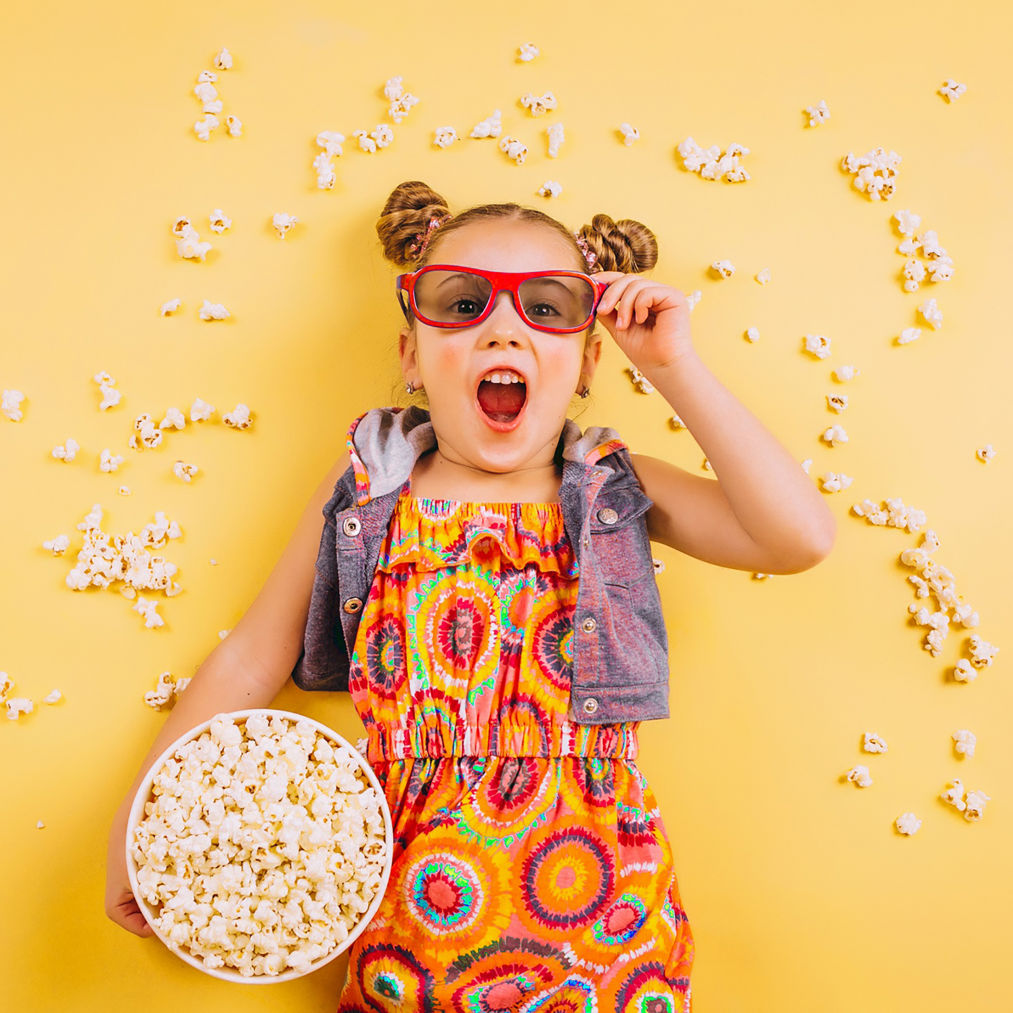 Ragazza con occhiali 3D, popcorn, espressione sorpresa, sfondo giallo, popcorn intorno.