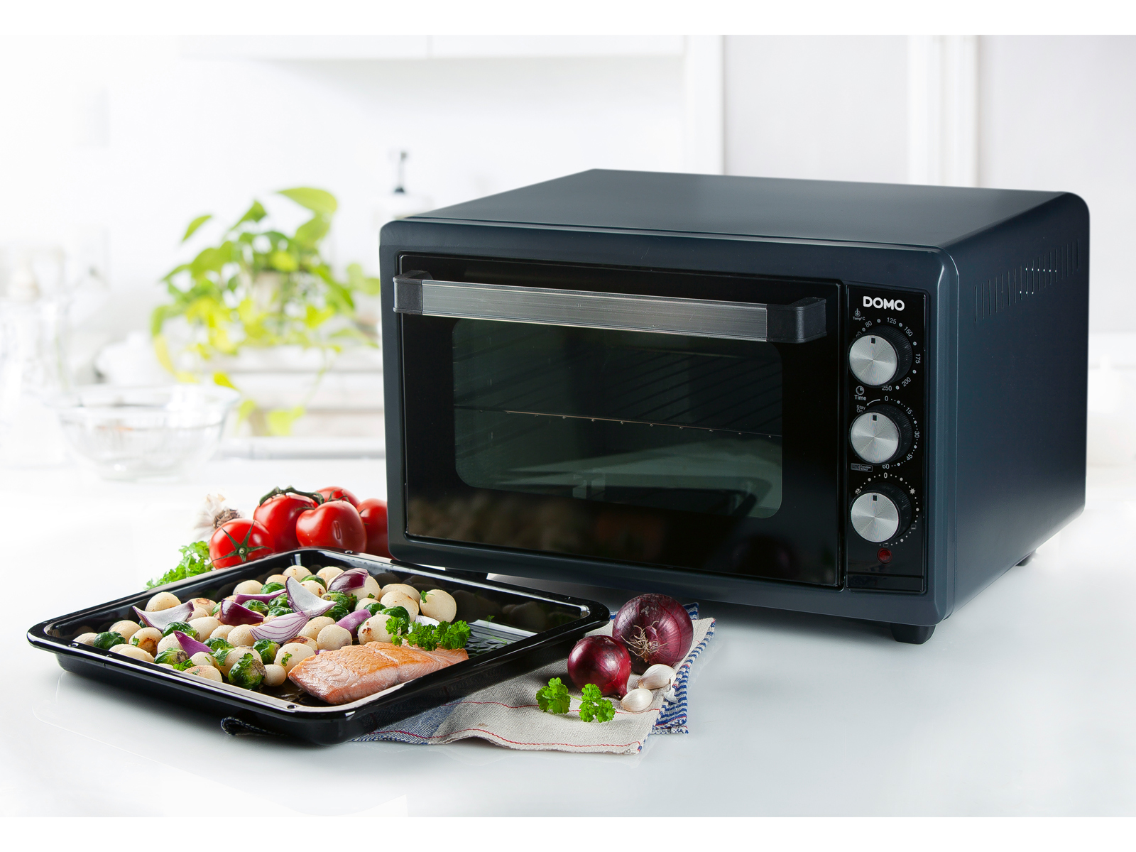 Piekarnik z tacą z jedzeniem. Pomidory, cebula i pieczarki na blacie.