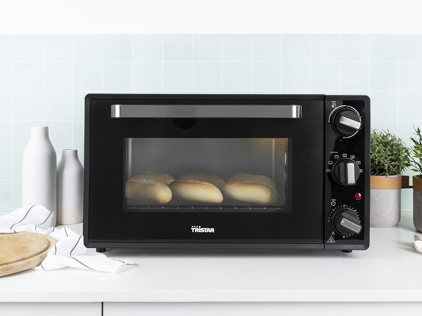 Czarny piekarnik z przeszklonymi drzwiami, pokazujący cztery bochenki chleba. Pokrętła i kontrolki po prawej stronie.