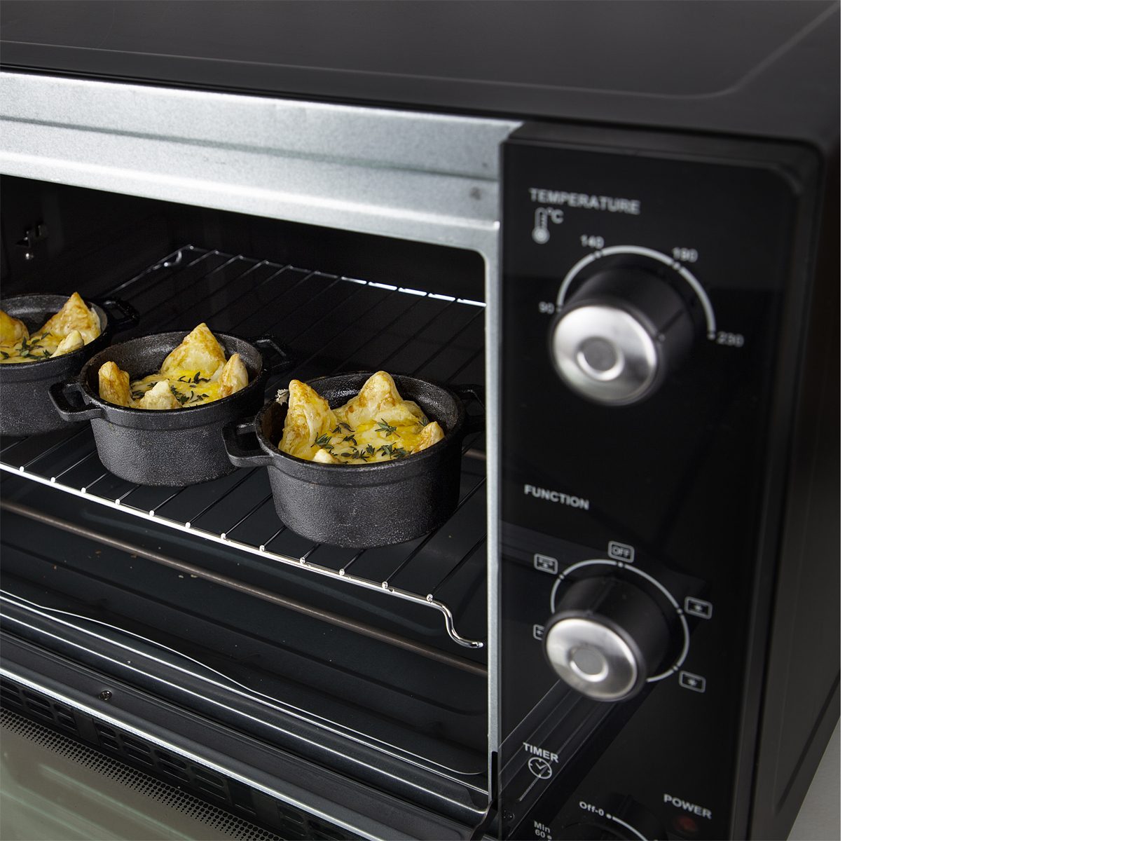 Vue intérieure du four avec trois petits plats avec nourriture sur une grille. La porte du four est ouverte, four noir.