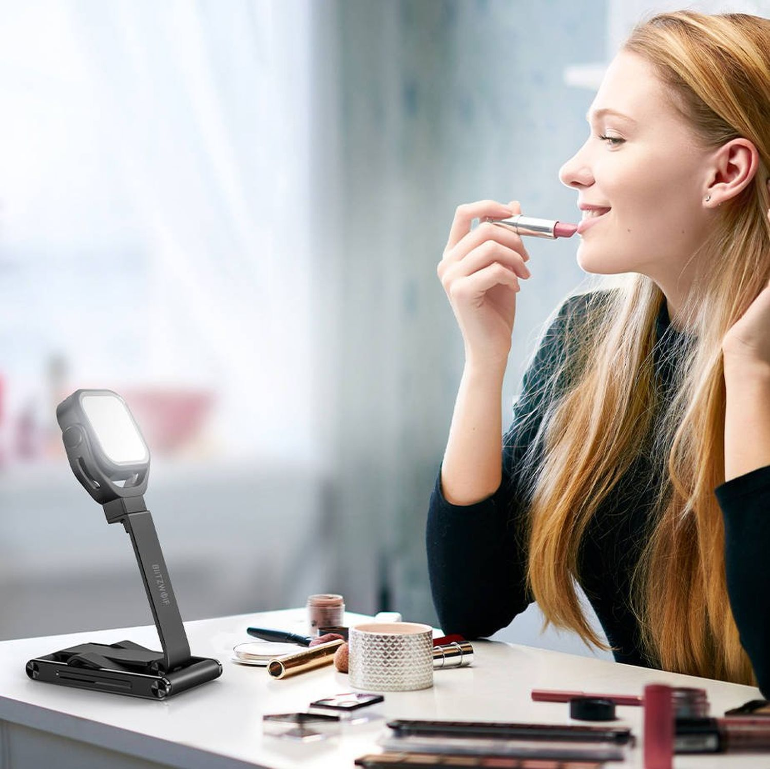Frau trägt Lippenstift auf, verwendet einen beleuchteten Schminkspiegel auf einem weißen Tisch.
