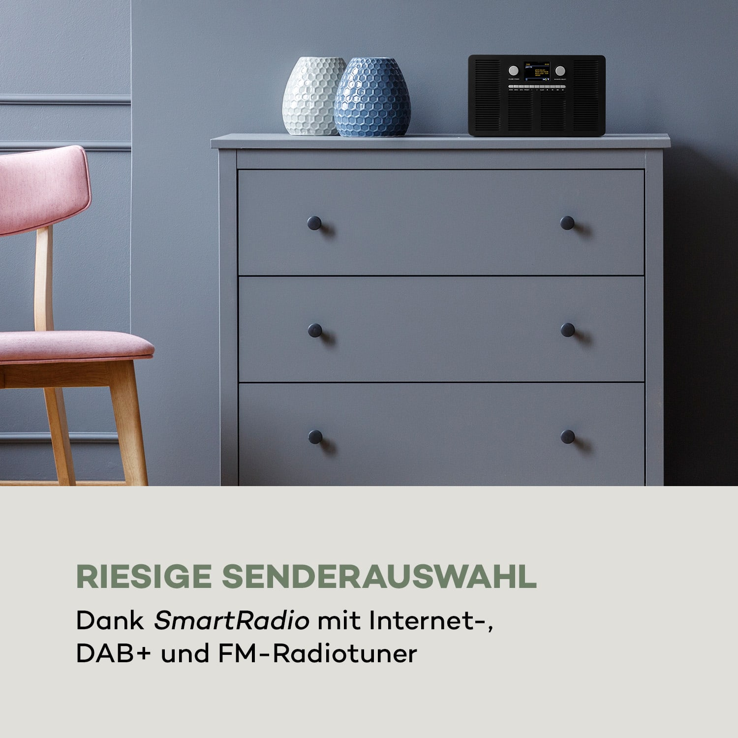 Graue Kommode mit Vasen und Radio. Rosa Stuhl. Text: RIESIGE SENDERAUSWAHL.