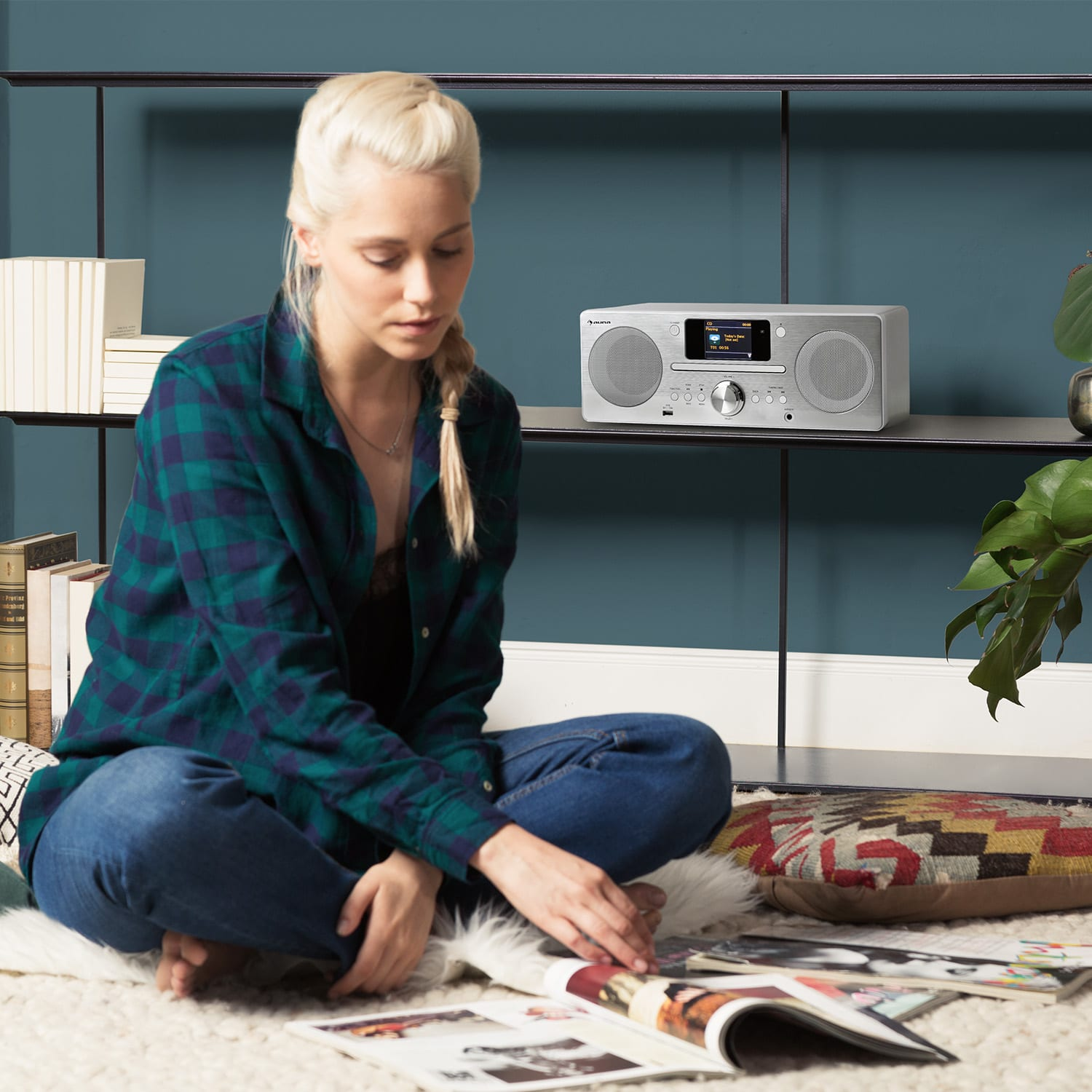 Blonde Frau mit Radio, Büchern und Zeitschriften. Auf einem Teppich sitzend.