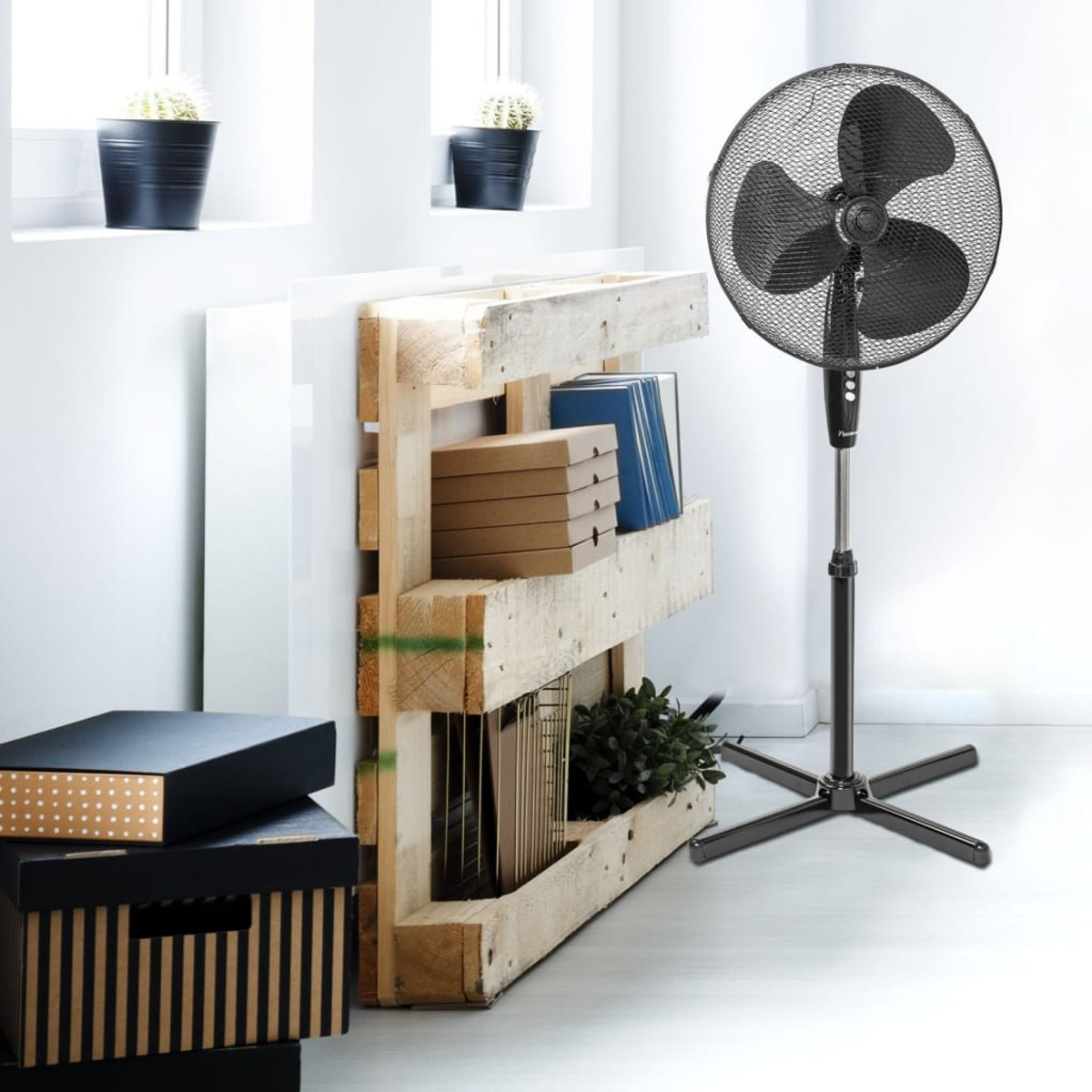 Czarny wentylator stojący z pudełkami na półce. Drewniana półka z palet z roślinami.