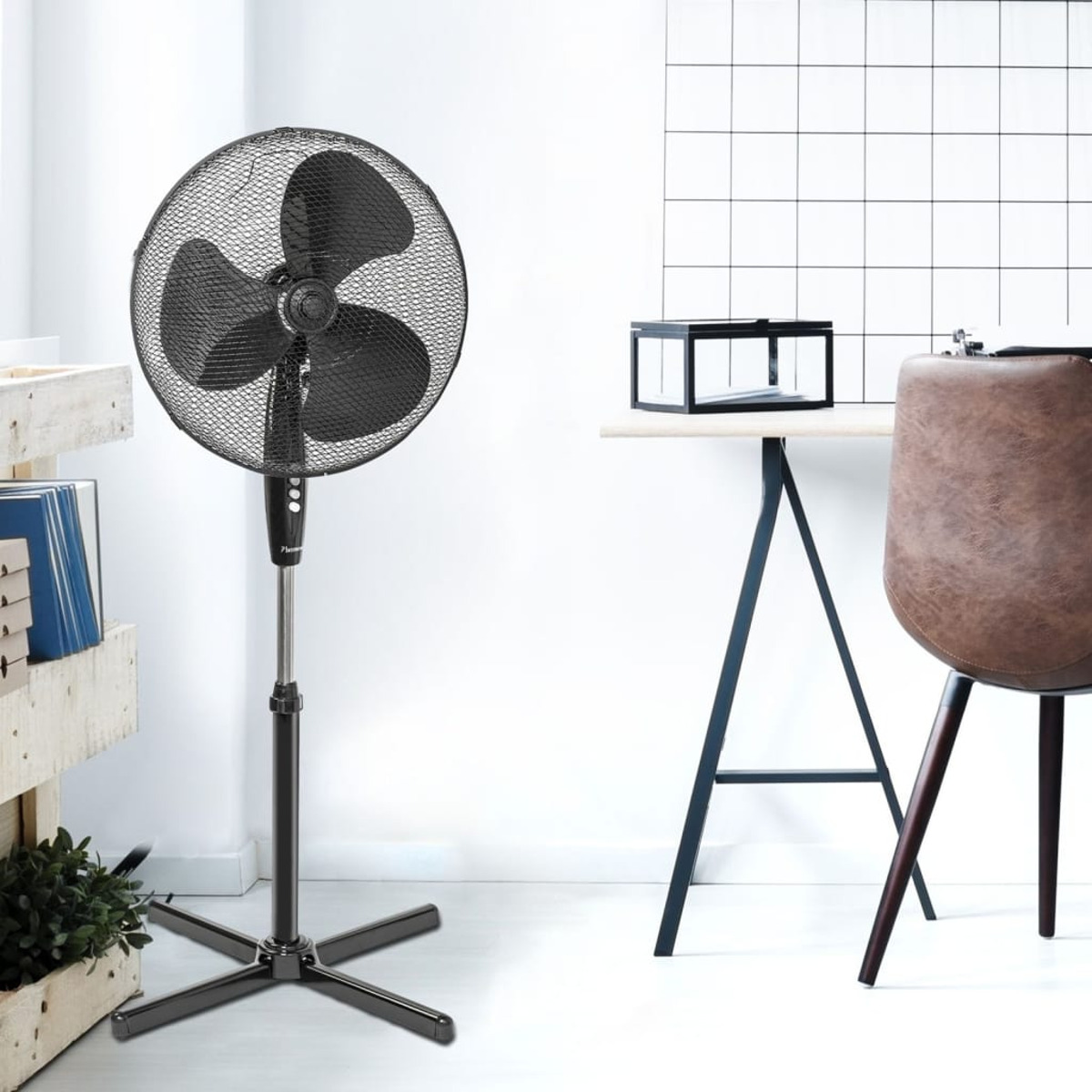 Czarny wentylator z trzema łopatkami, na stojaku, w białym pokoju z biurkiem i krzesłem.