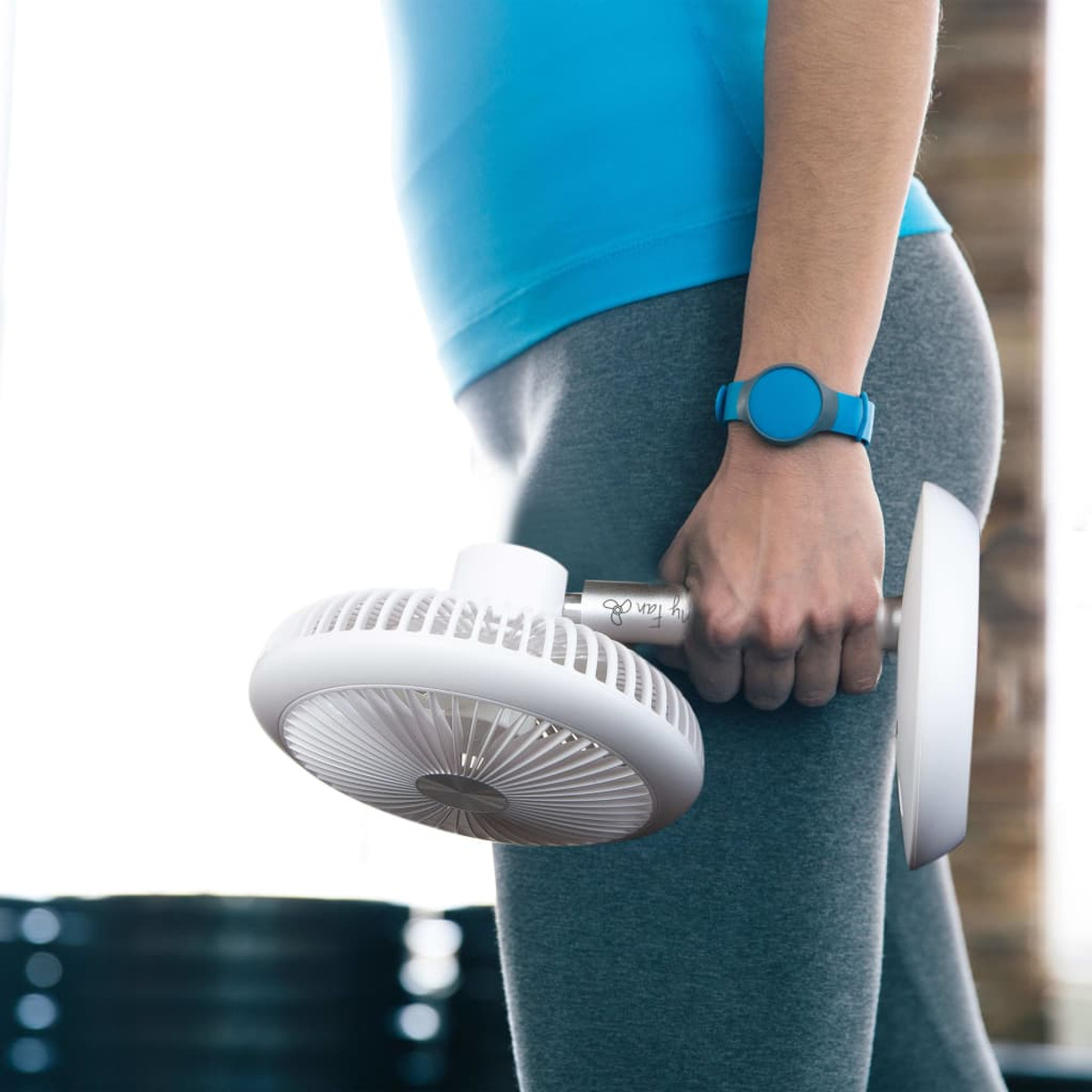 Person hält weißen Ventilator mit Griff, trägt Sportkleidung.