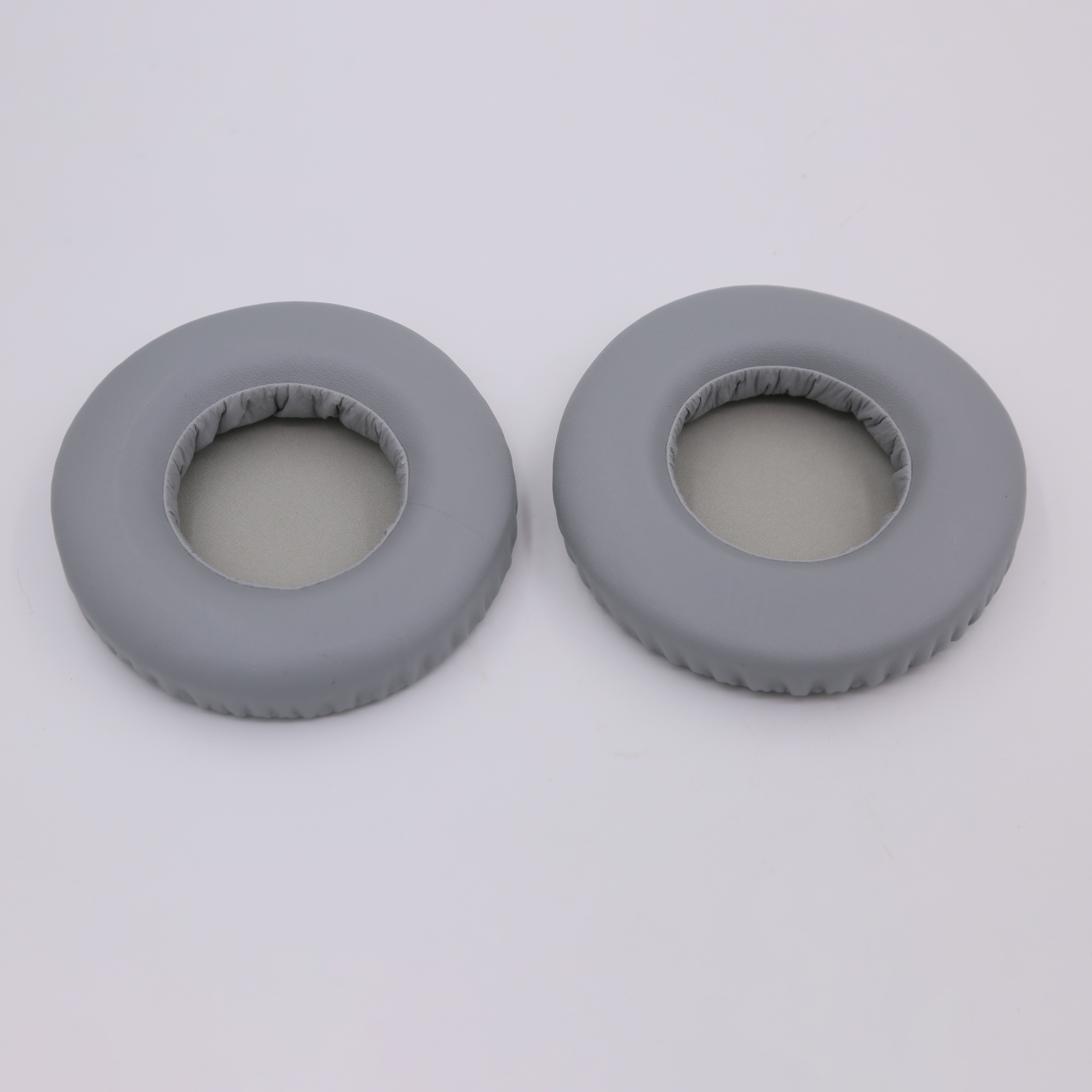 Zwei graue Ohrpolster auf weißer Oberfläche. Die Ohrpolster sind kreisförmig.
