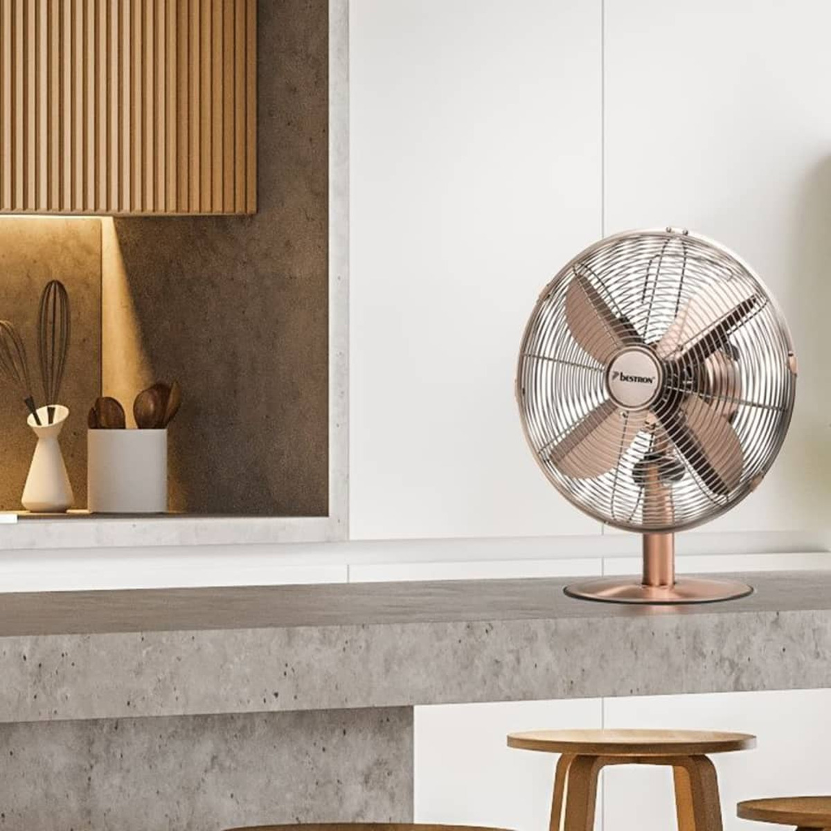 Un ventilatore Bestron color oro rosa è su un piano di lavoro in cemento in una cucina. Elementi in legno sullo sfondo.