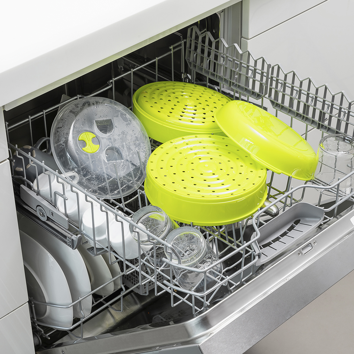 Un lavavajillas con platos, vasos y recipientes verdes en su interior.