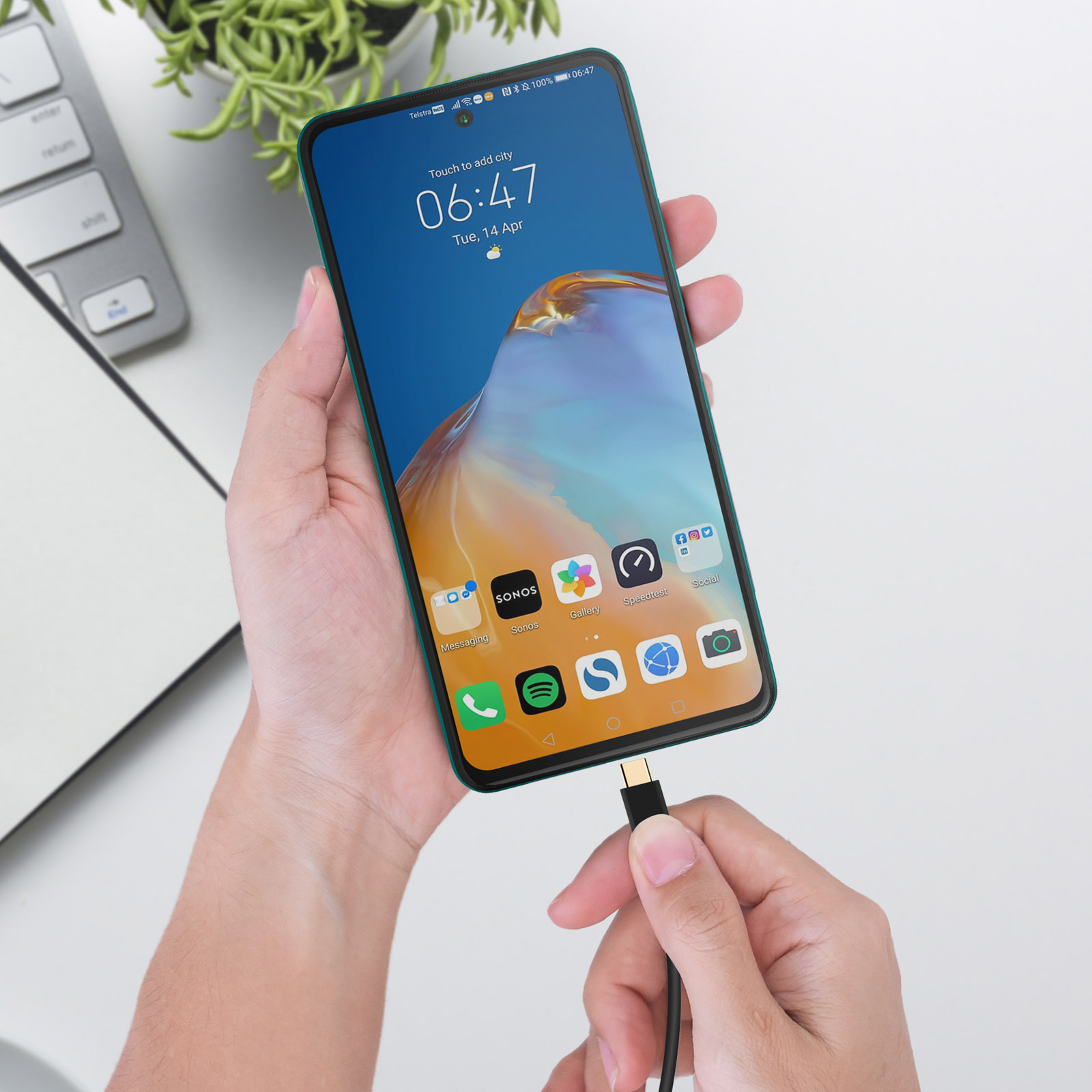 Mano che tiene uno smartphone, collegato a un cavo di ricarica. Telefono mostra icone app.