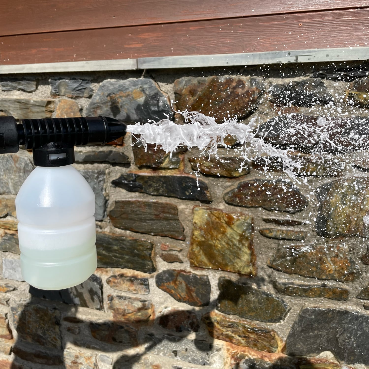 Una hidrolavadora rociando espuma blanca contra una pared de piedra.