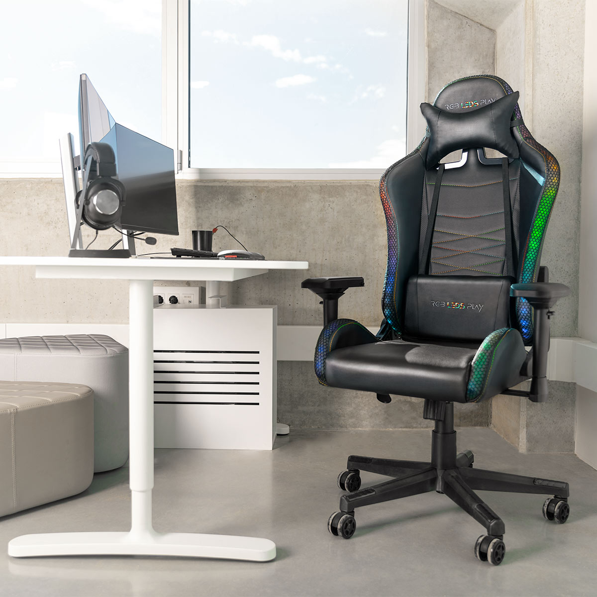 Configuración de juego: silla negra, escritorio con monitor, auriculares y ventana de fondo. Suelo gris.