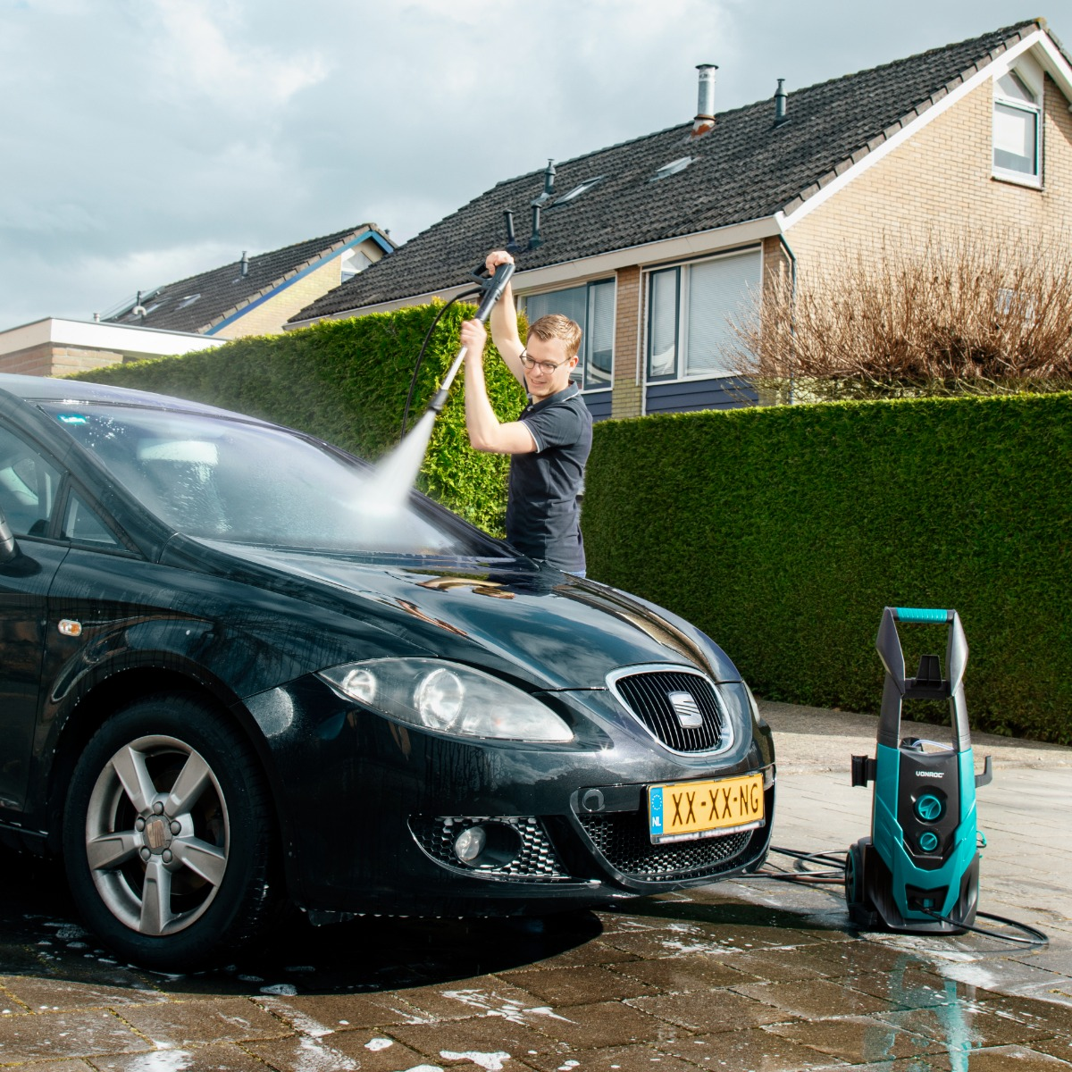 Man wast een zwarte auto met een hogedrukreiniger op een zonnige dag.