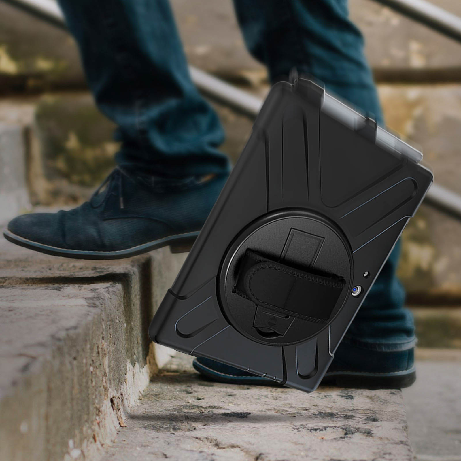 Füße einer Person auf Treppen, die eine schwarze Tablethülle mit Handschlaufe halten.
