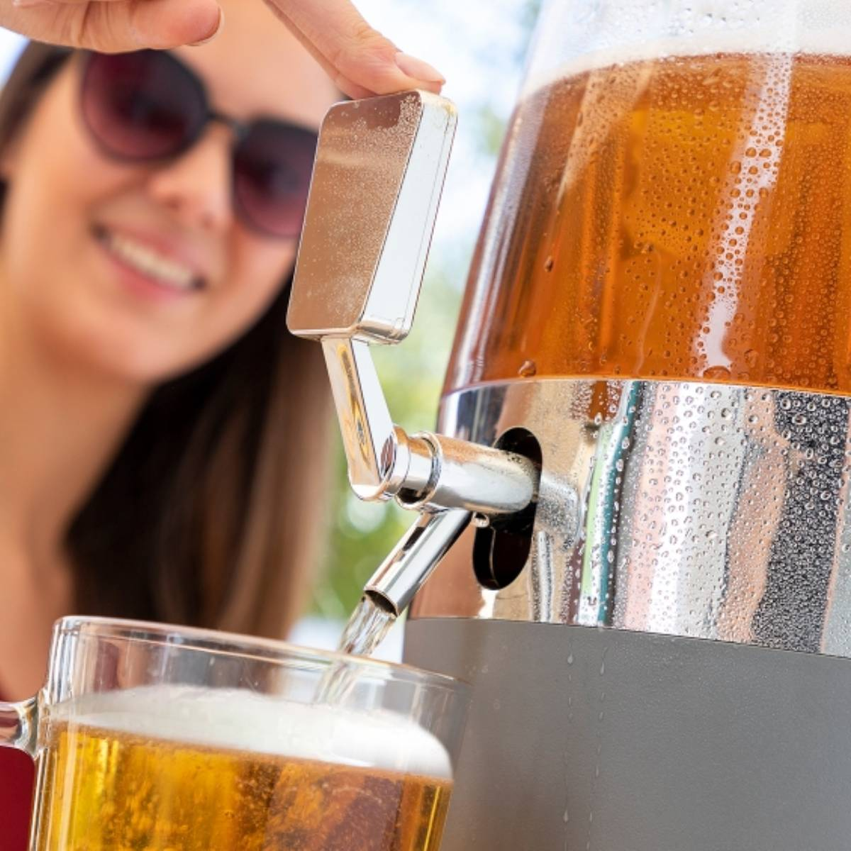 Una donna versa birra da un distributore in un bicchiere. La birra è dorata.