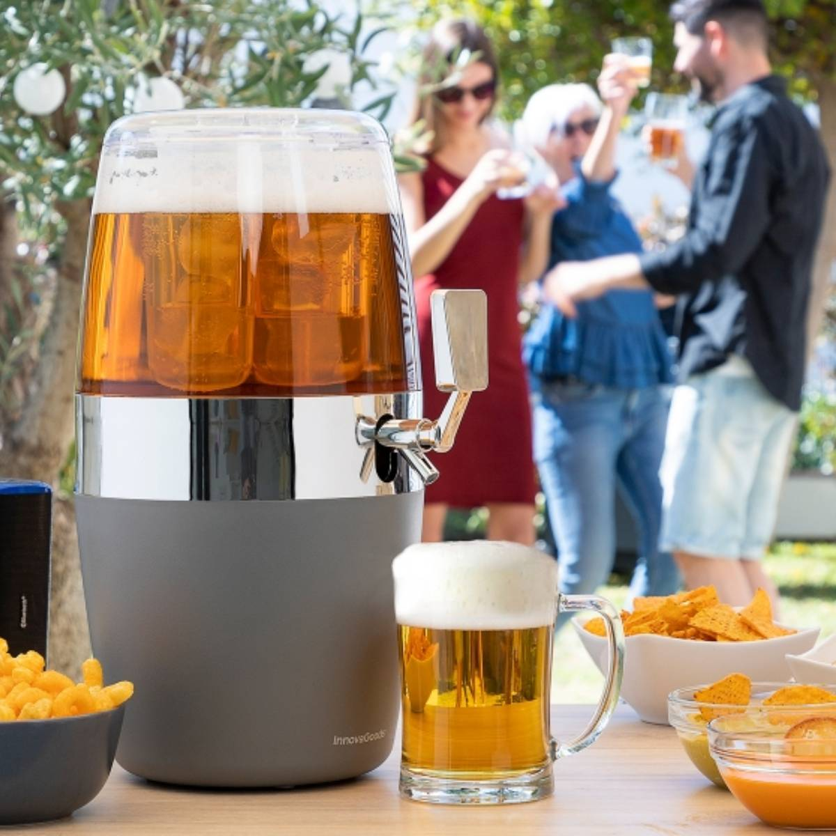 Erogatore di birra con persone, birra in una tazza e snack su un tavolo all'aperto.