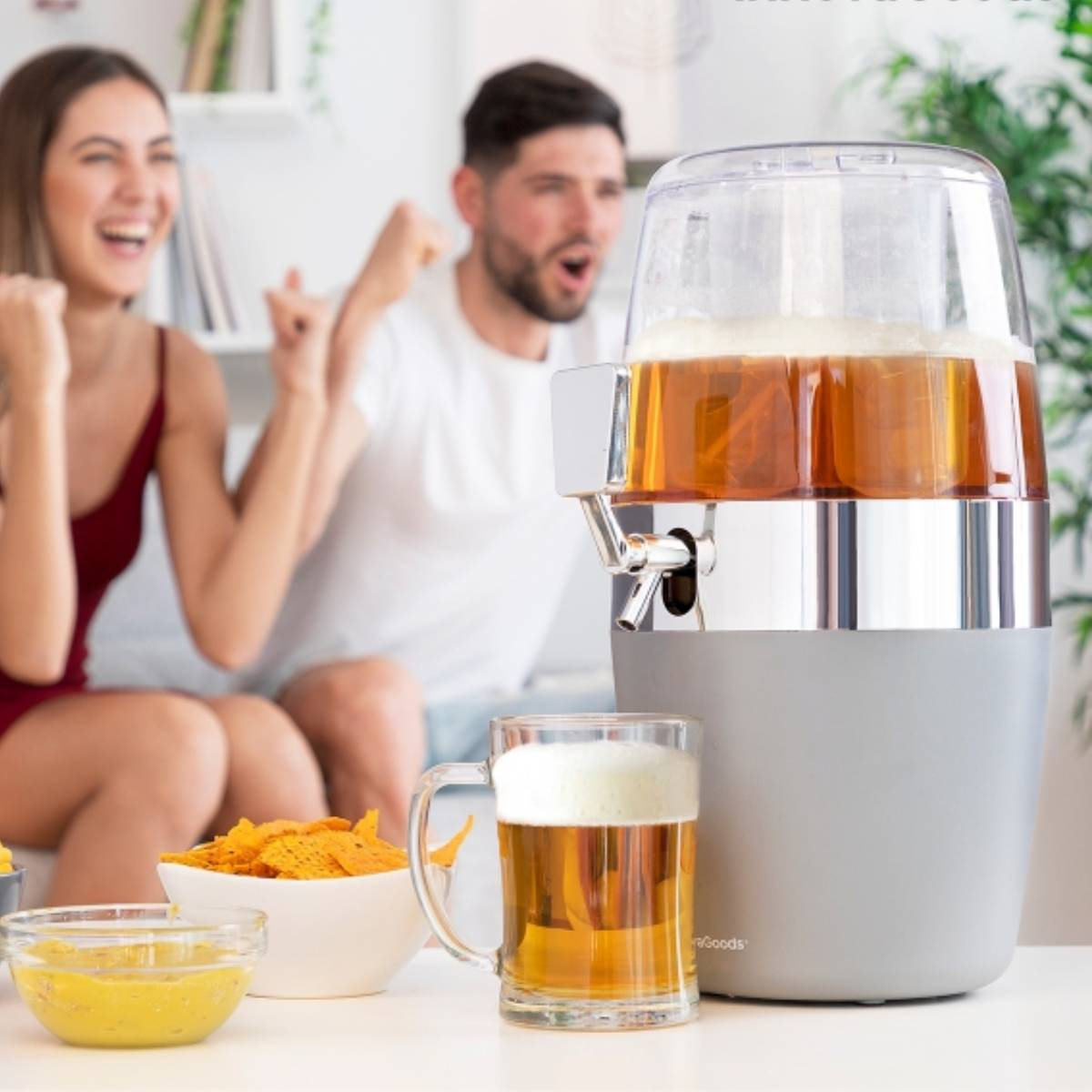 Un distributore di birra su un tavolo, con un boccale e snack. Persone eccitate sullo sfondo.
