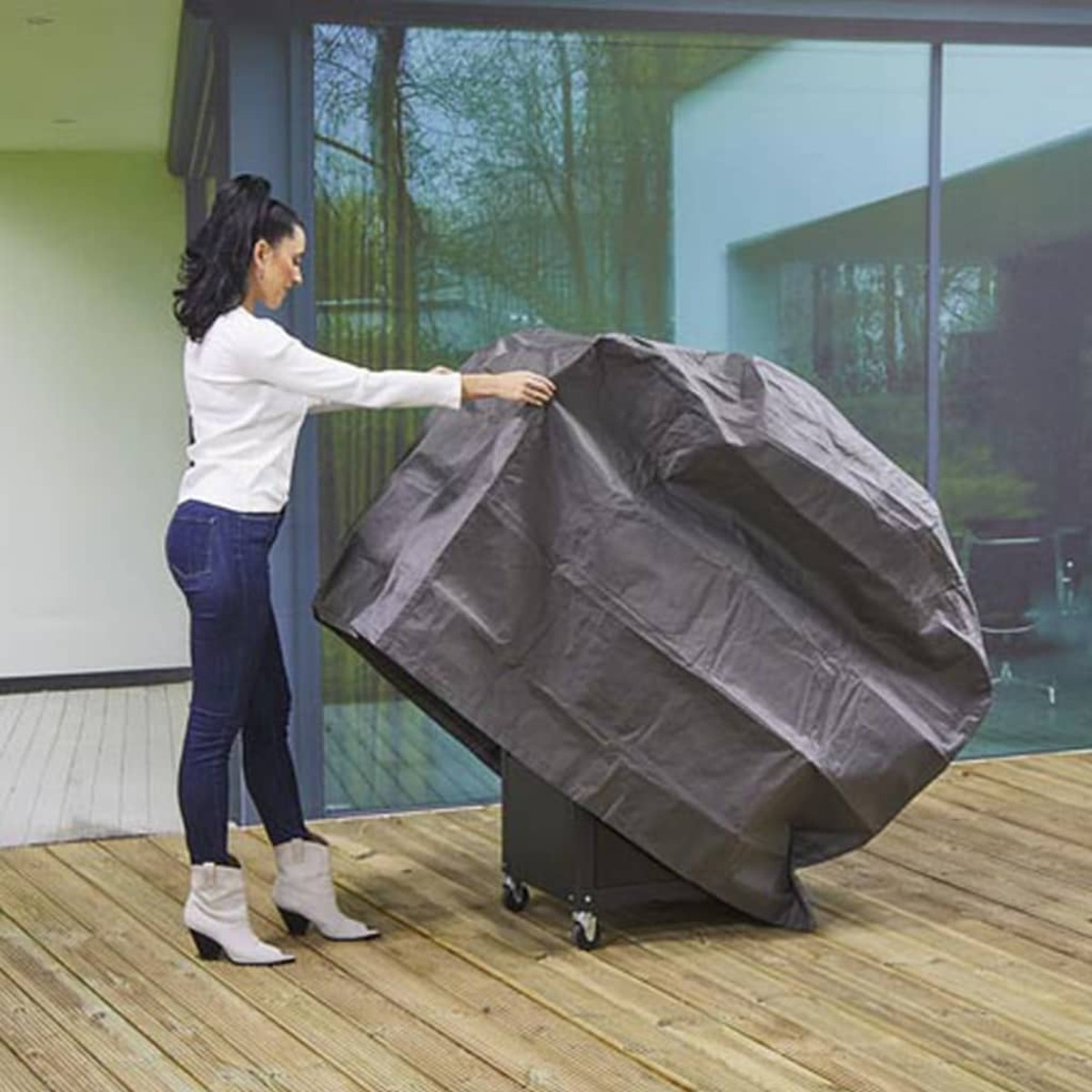 Donna che copre un grill con una copertura grigio scuro su un ponte di legno.