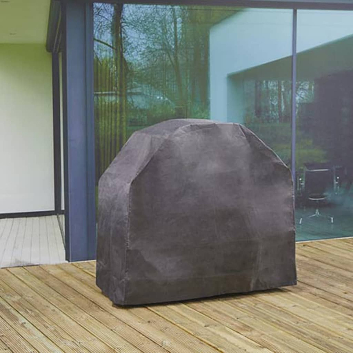 Eine dunkelgraue Grillabdeckung auf einer Holzterrasse, mit Glaswand und Bäumen im Hintergrund.