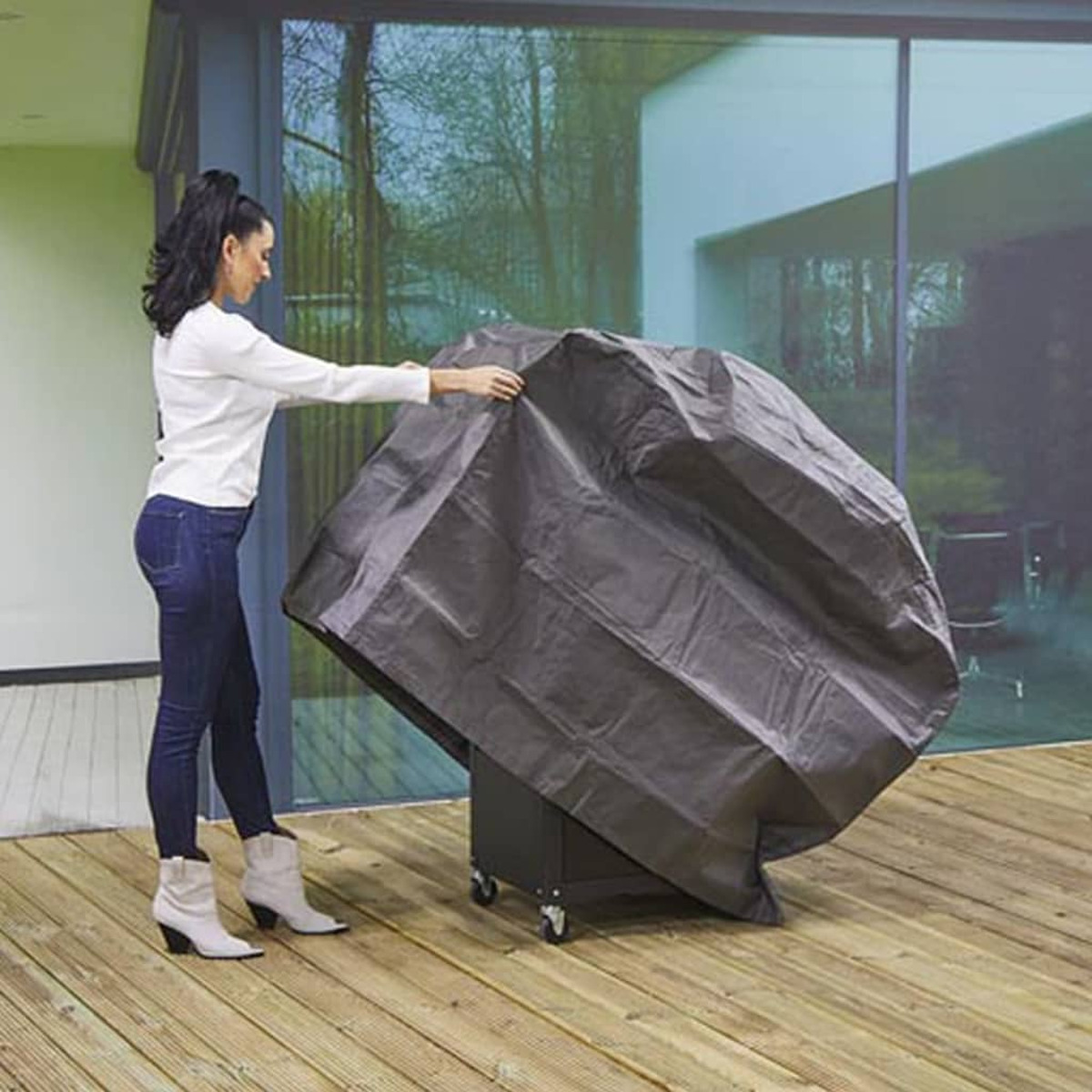 Eine Frau deckt einen Grill mit einer dunklen Abdeckung auf einem Holzdeck ab.