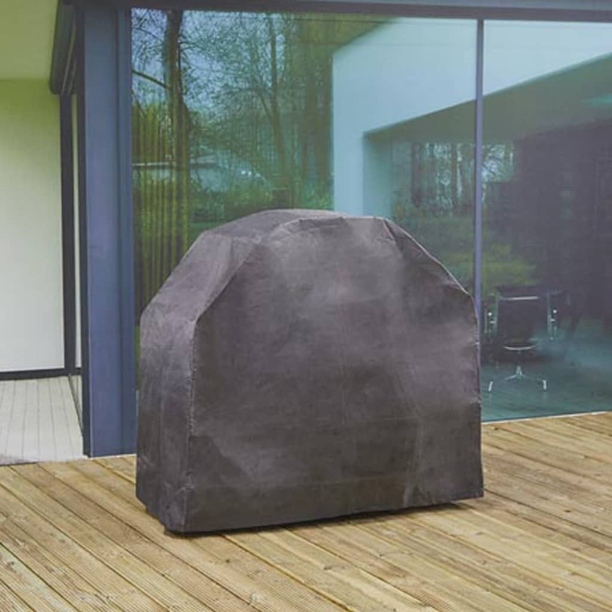 Eine graue Abdeckung über einem Grill auf einer Holzterrasse, in der Nähe einer Glastür und eines Hauses.