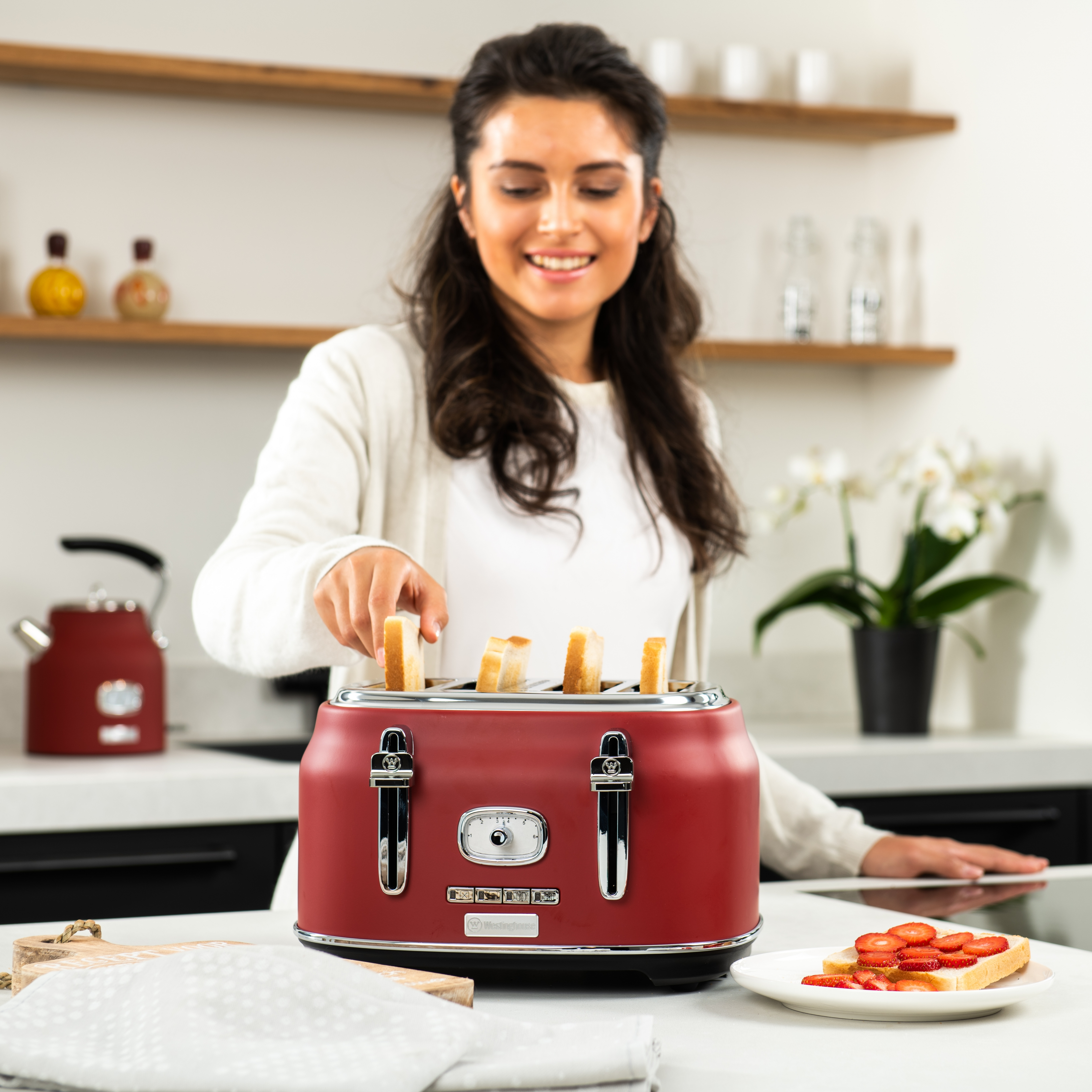 Frau legt Brot in roten Retro-Toaster auf weißer Küchenzeile.