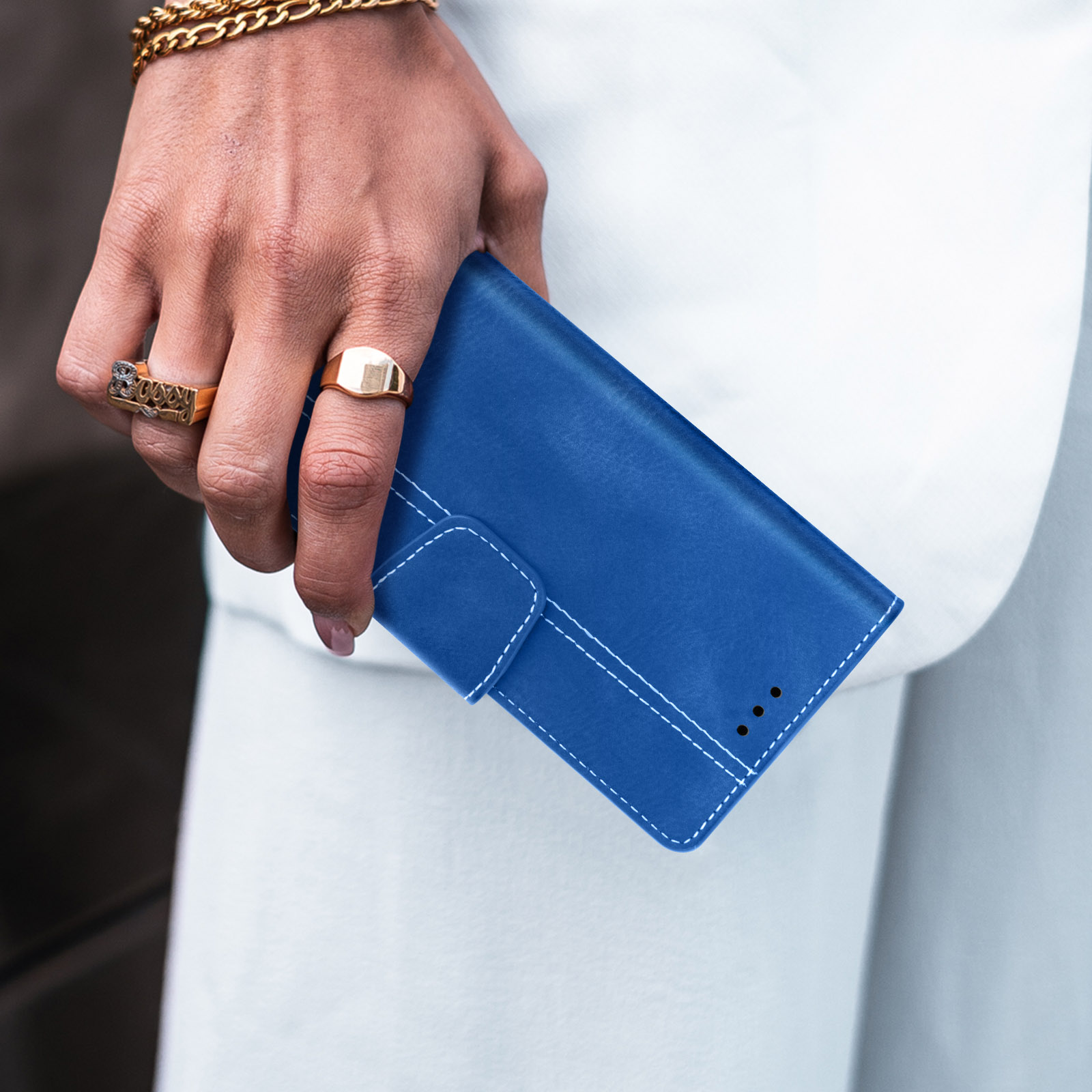 Person hält blaue Leder-Handyhülle mit goldenen Ringen.