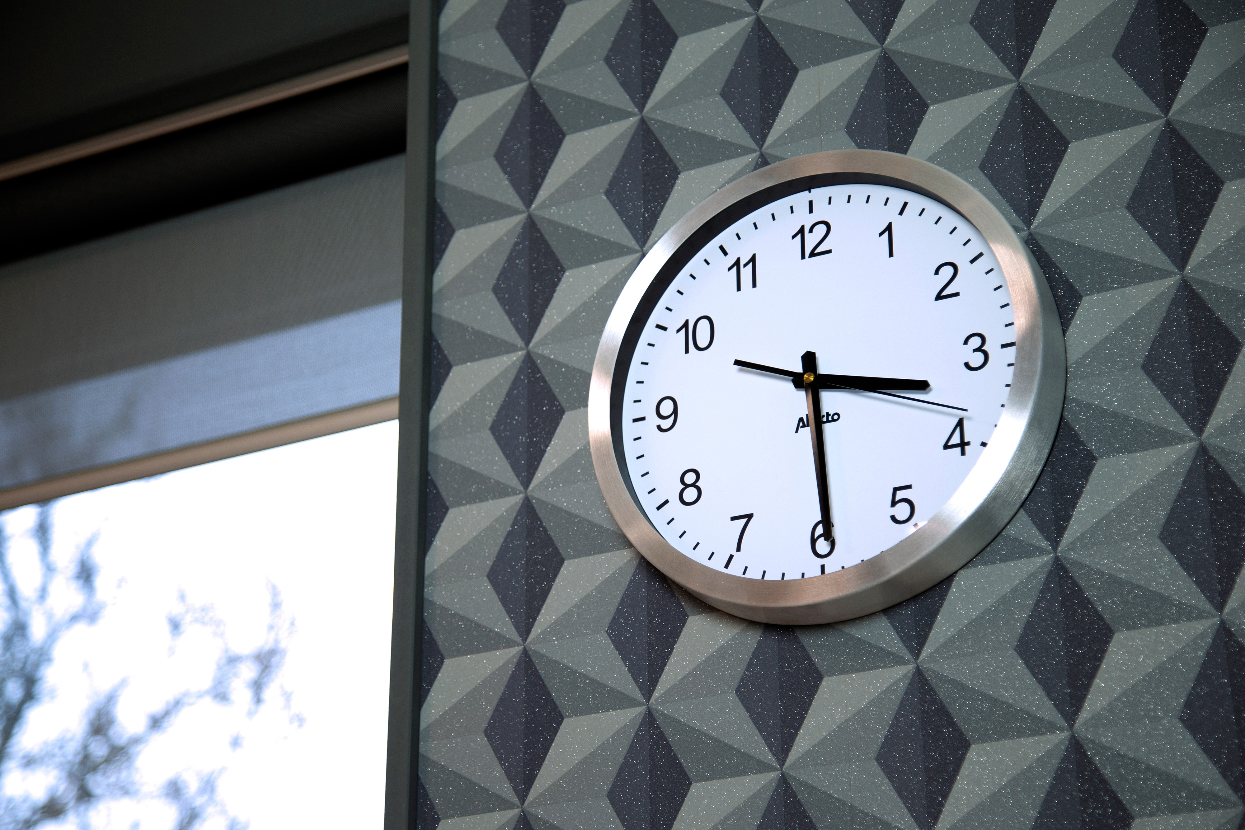 Eine Uhr zeigt 2:15 Uhr. Sie ist rund, silber gerahmt, mit weißem Zifferblatt und schwarzen Zeigern, an einer Wand.